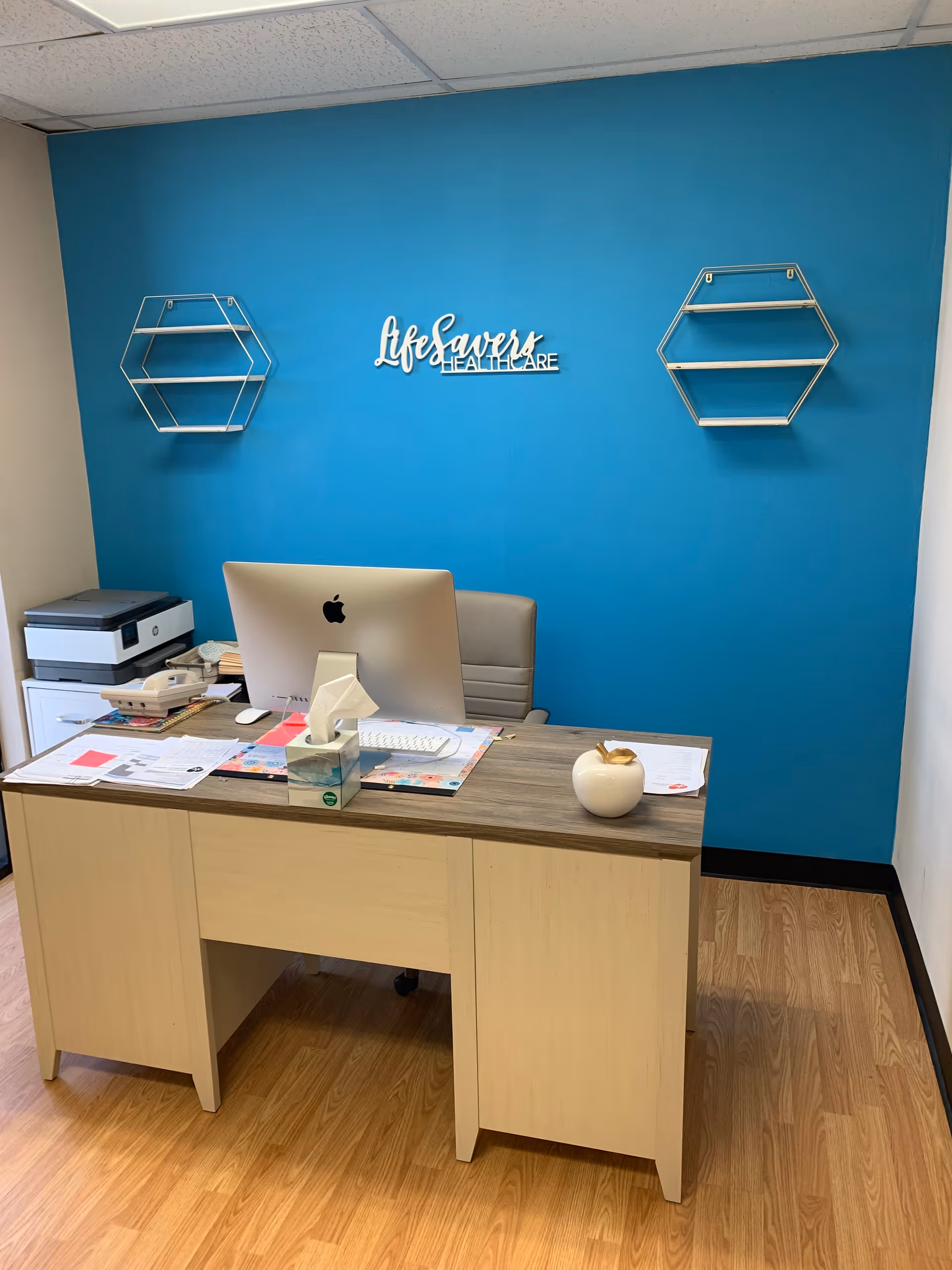 Office desk with iMac, blue wall, and decorative shelves at LifeSavers Healthcare.