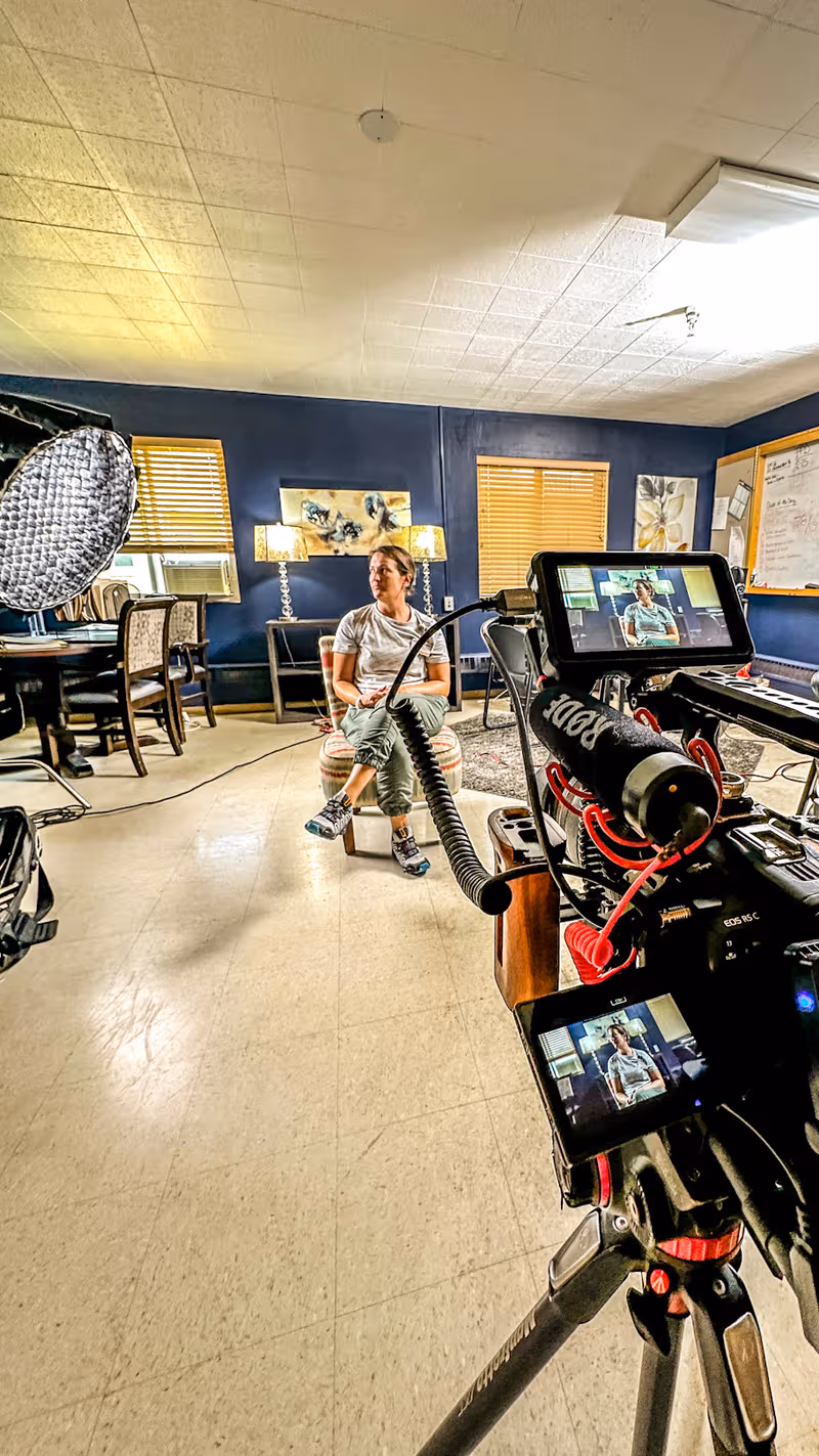 Resident seated in a blue-walled lounge as filming equipment records the scene.