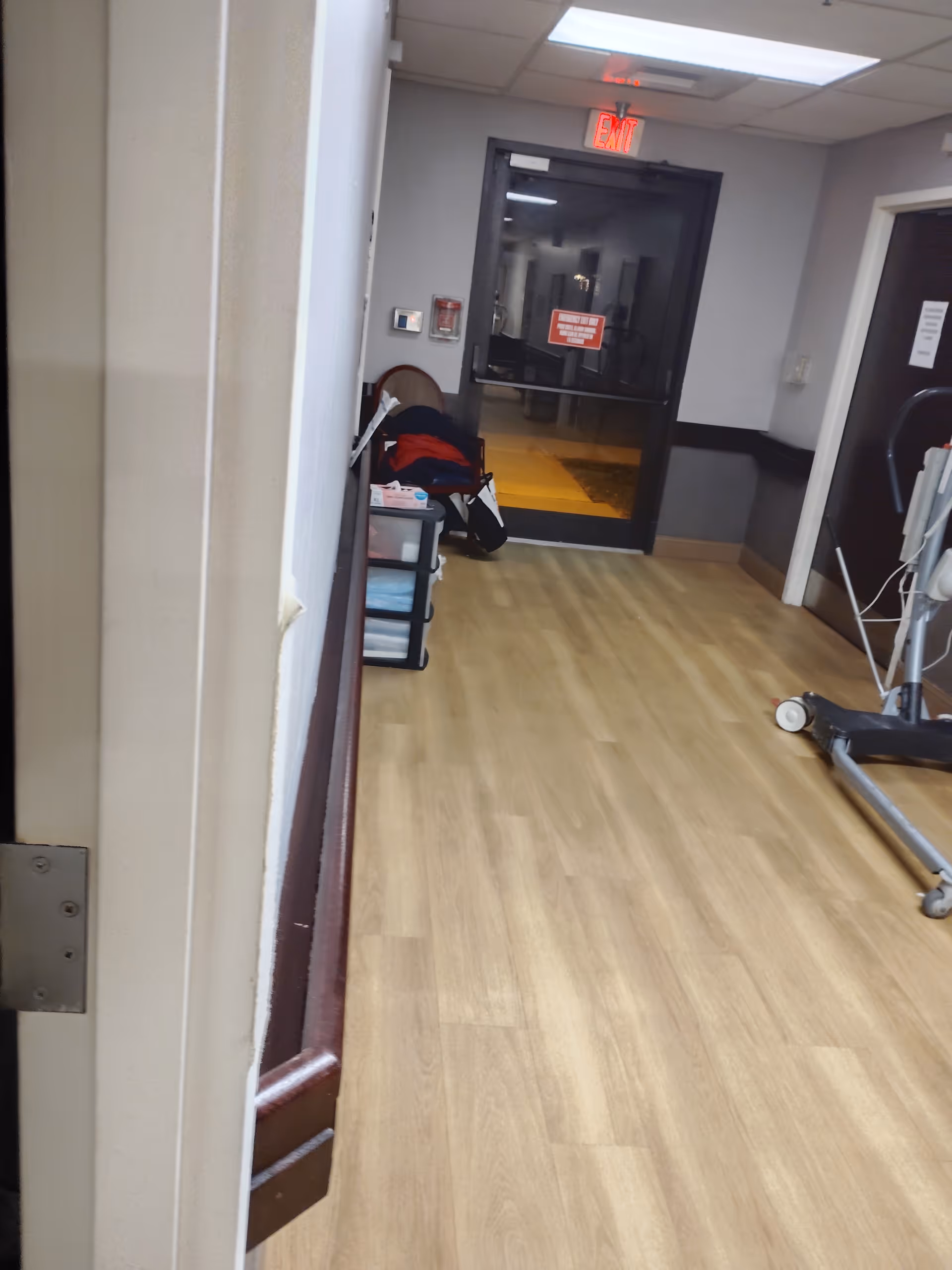 Indoor hallway in a senior living facility with a glass door at the end and equipment.