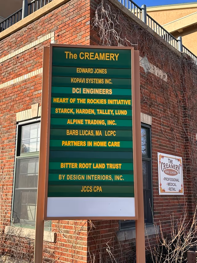 Exterior brick building with a green tenant signboard listing businesses outside.