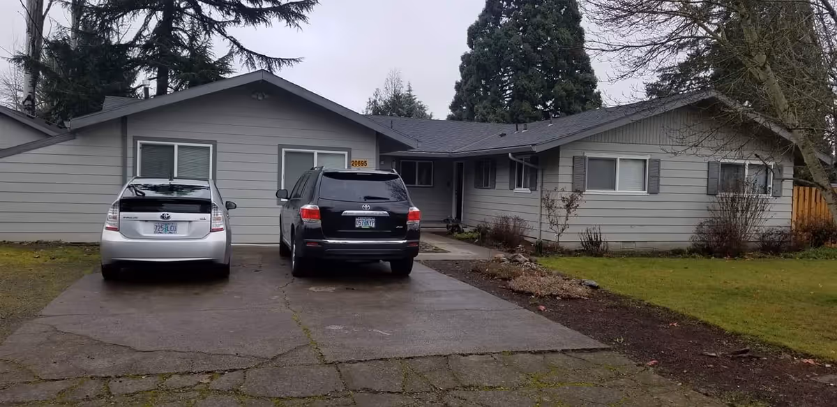 Front view of a single-story gray house with two parked cars in a driveway.