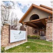 Front entrance of Millcreek Meadows building with stone pillars and a lawn sign displaying the facility name.