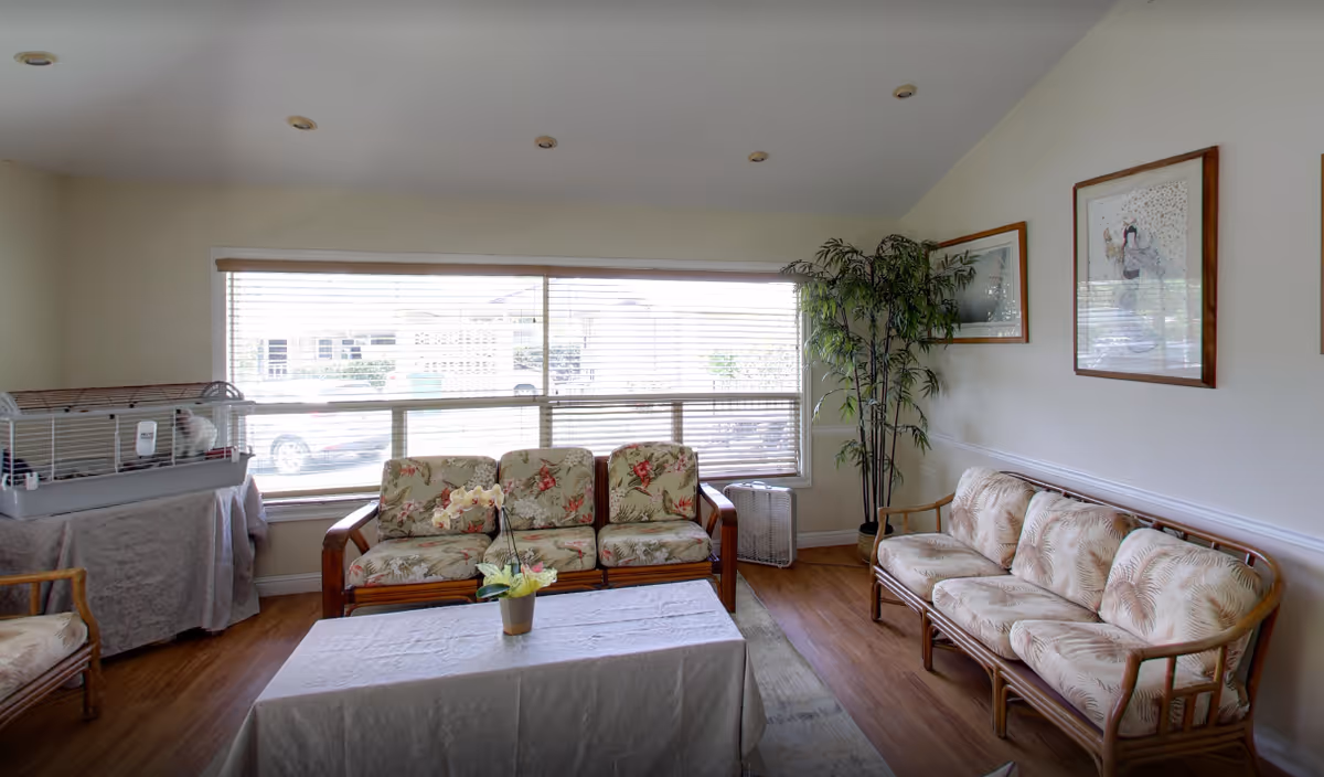 Bright senior living lounge with floral-patterned couches, a bird cage, and a large window.