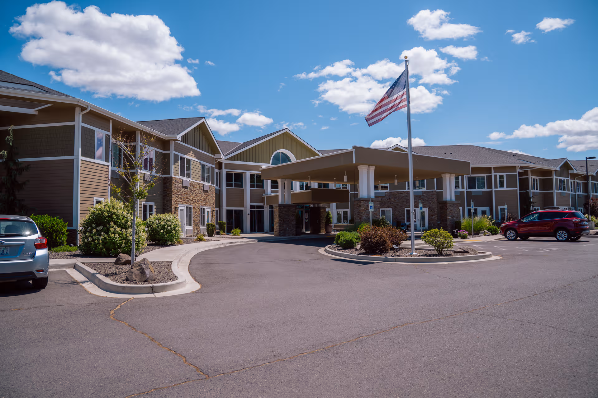 Exterior view of Fieldstone OrchardWest senior living facility with a covered entrance and flag.