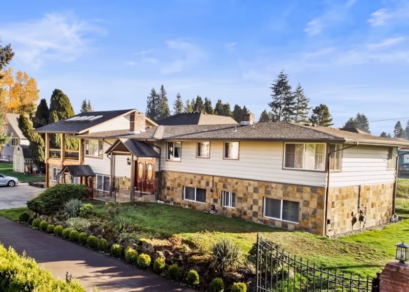 Two-story senior living building with stone base, light siding, and manicured front landscaping.