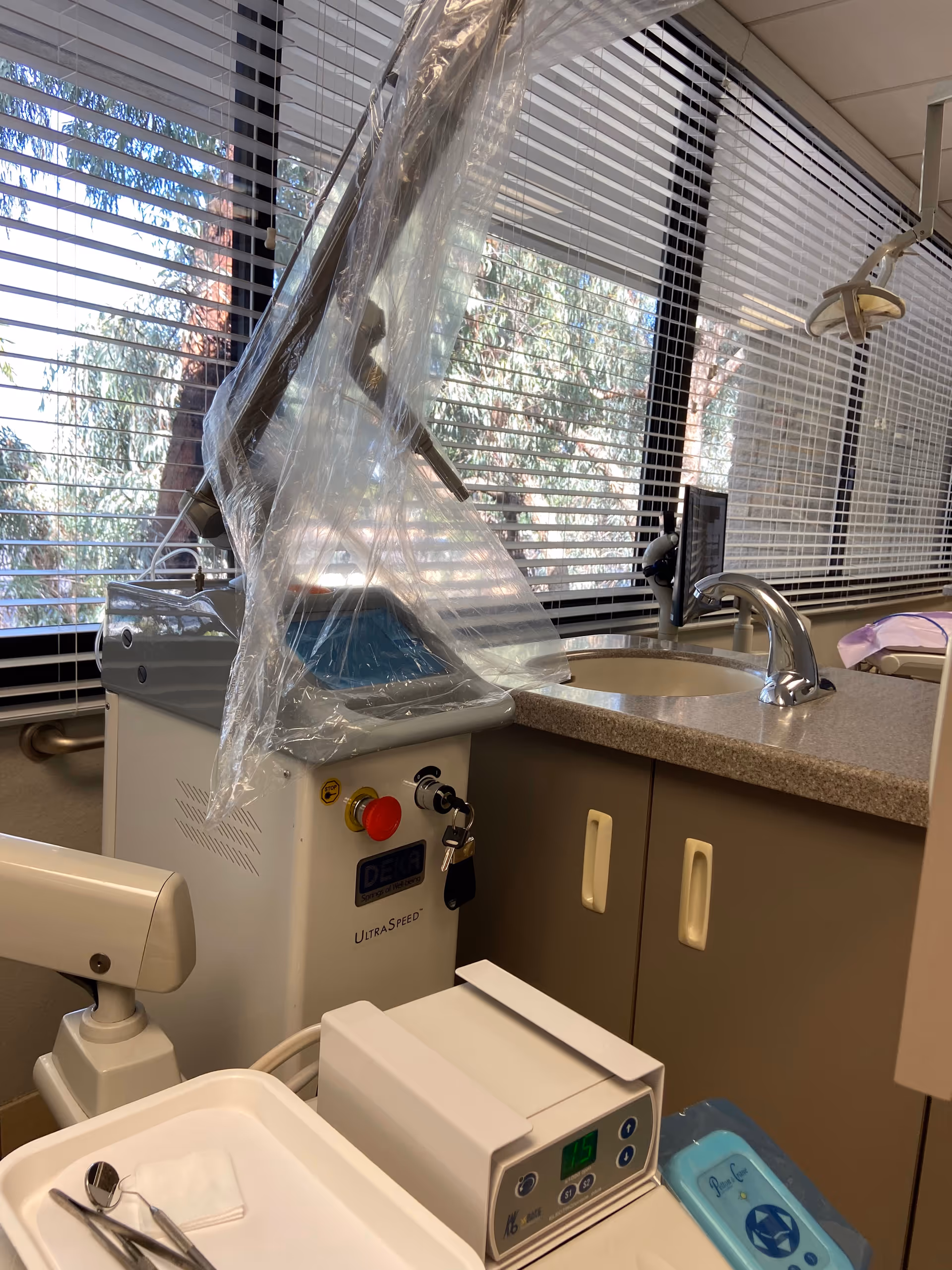 Dental treatment room with sink, cabinets, and a plastic-covered treatment device.