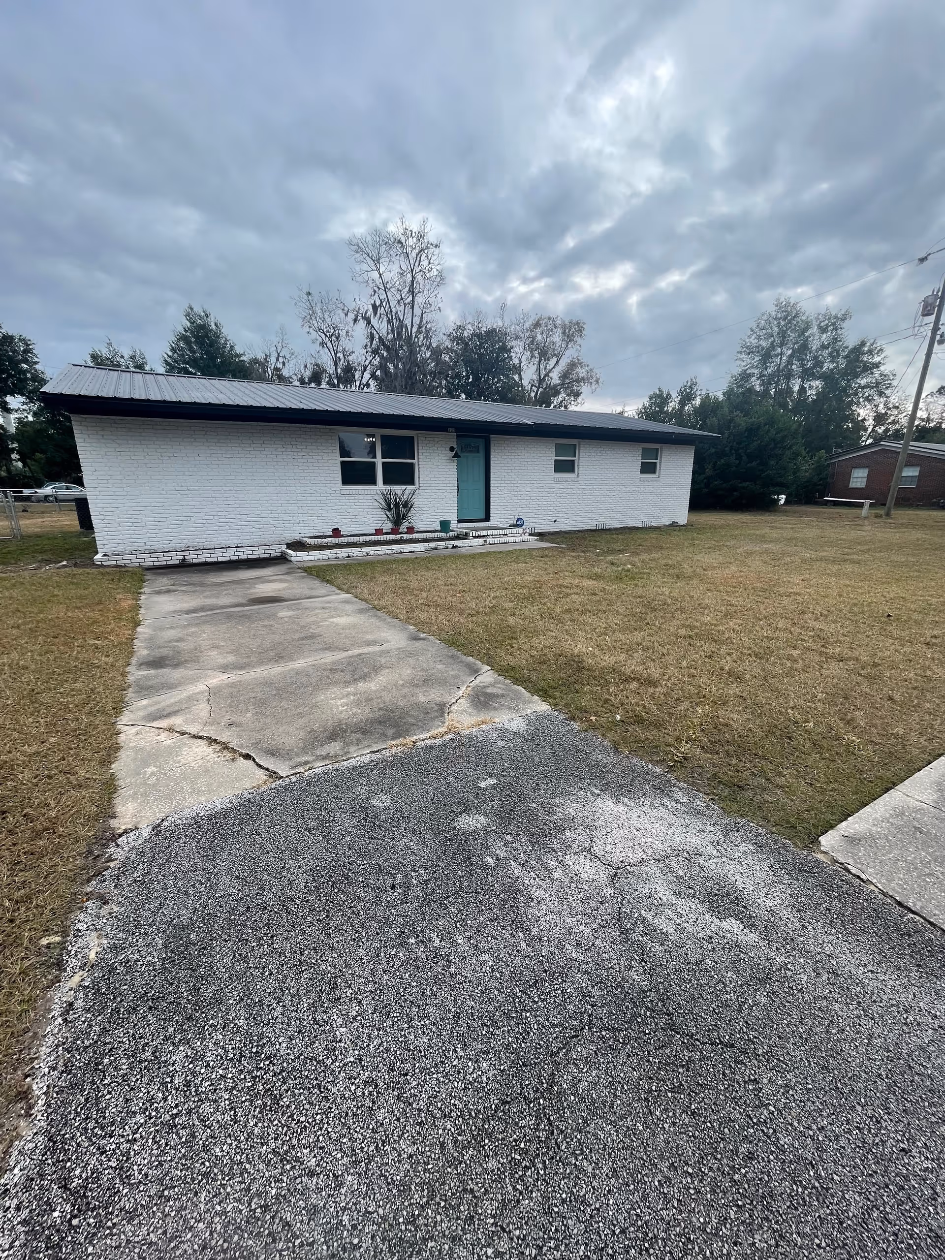 Single-story white brick facility with teal front door, walkway, and surrounding lawn.