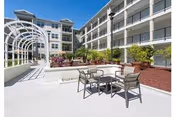 An outdoor courtyard with seating, planters, and a multi-story senior living building.