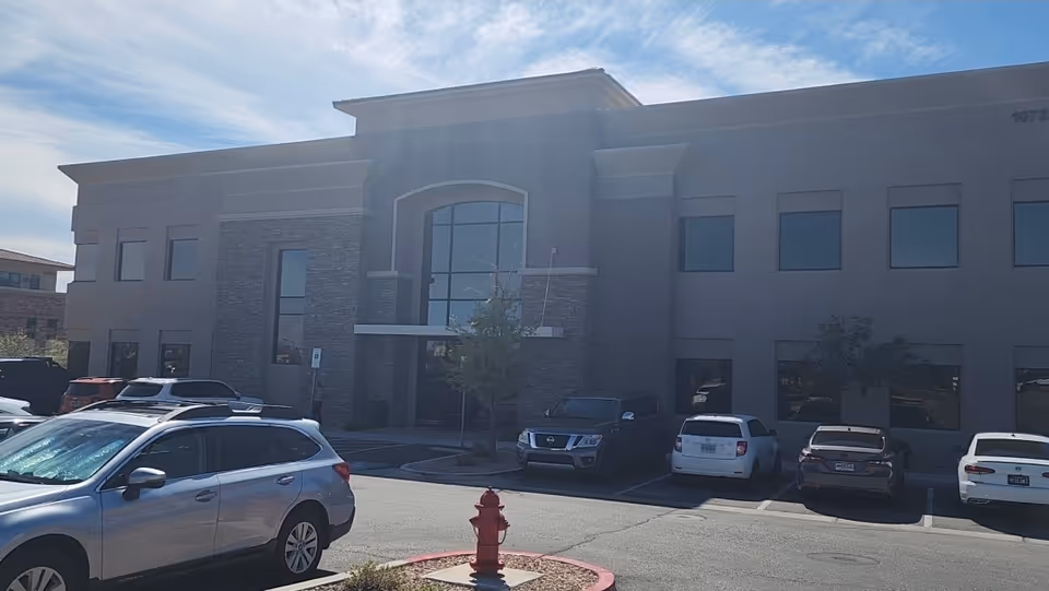 Modern two-story facility facade with arched entrance, stone accents, and parked cars in front.