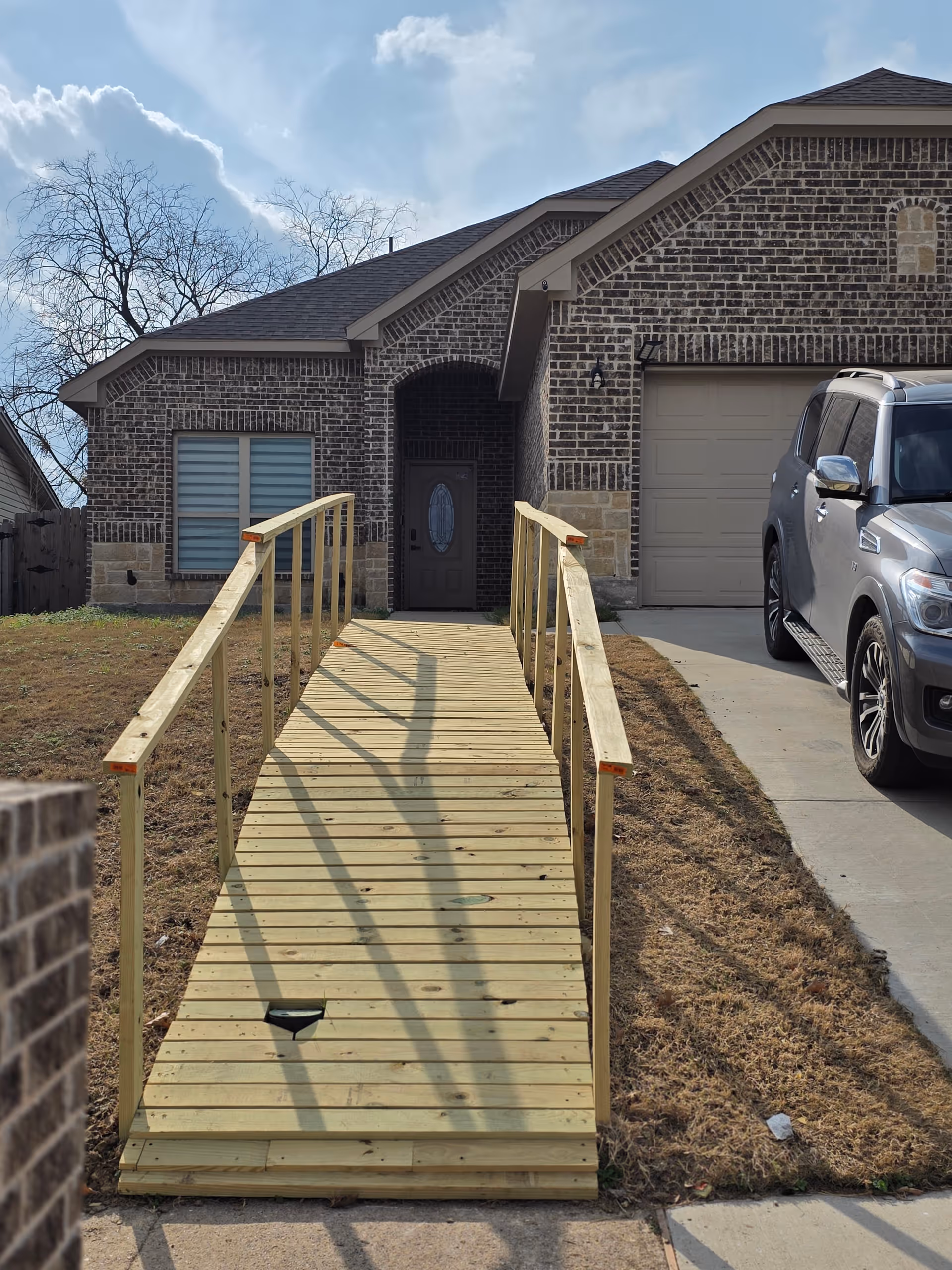 Front entrance of brick building with wooden accessibility ramp and SUV.