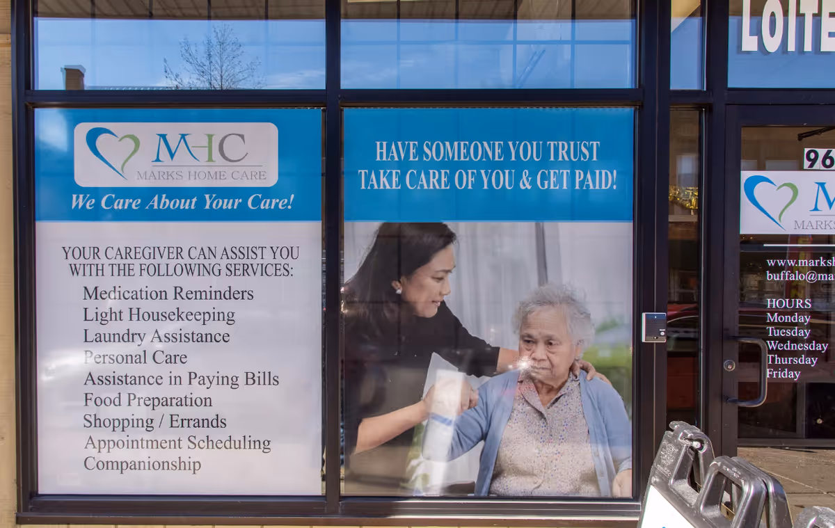 Storefront window shows banners for Marks Home Care with caregiver assisting elderly woman.