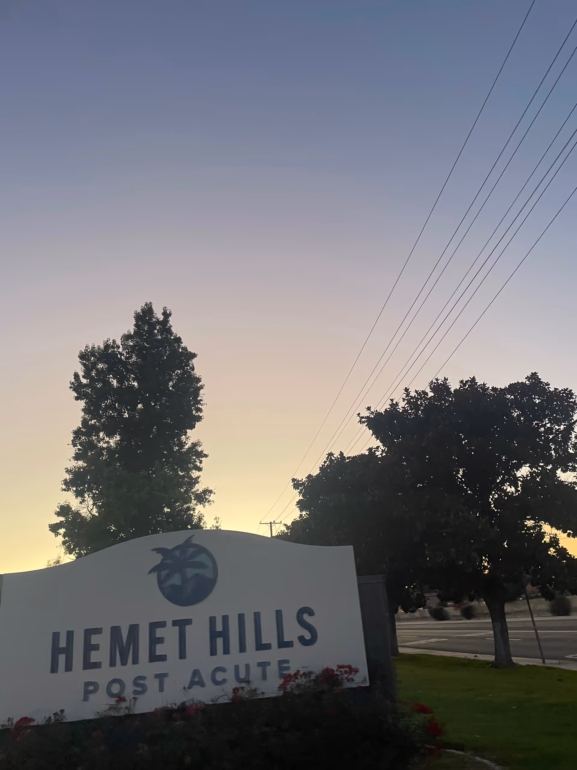 Exterior view of Hemet Hills Post Acute sign beside trees at dusk.