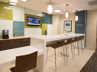 Bright dining area with a long white counter, brown stools, and a wall-mounted TV.