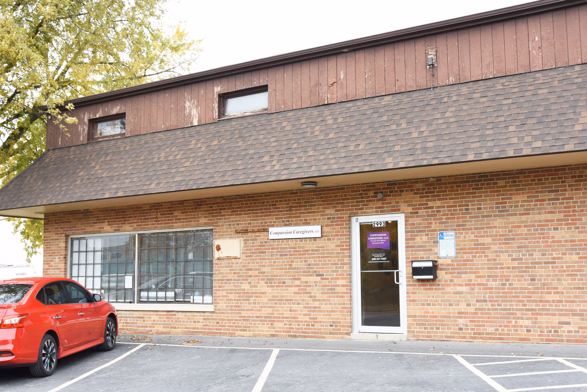 Brick building with a glass door entrance and a red car in the parking lot.