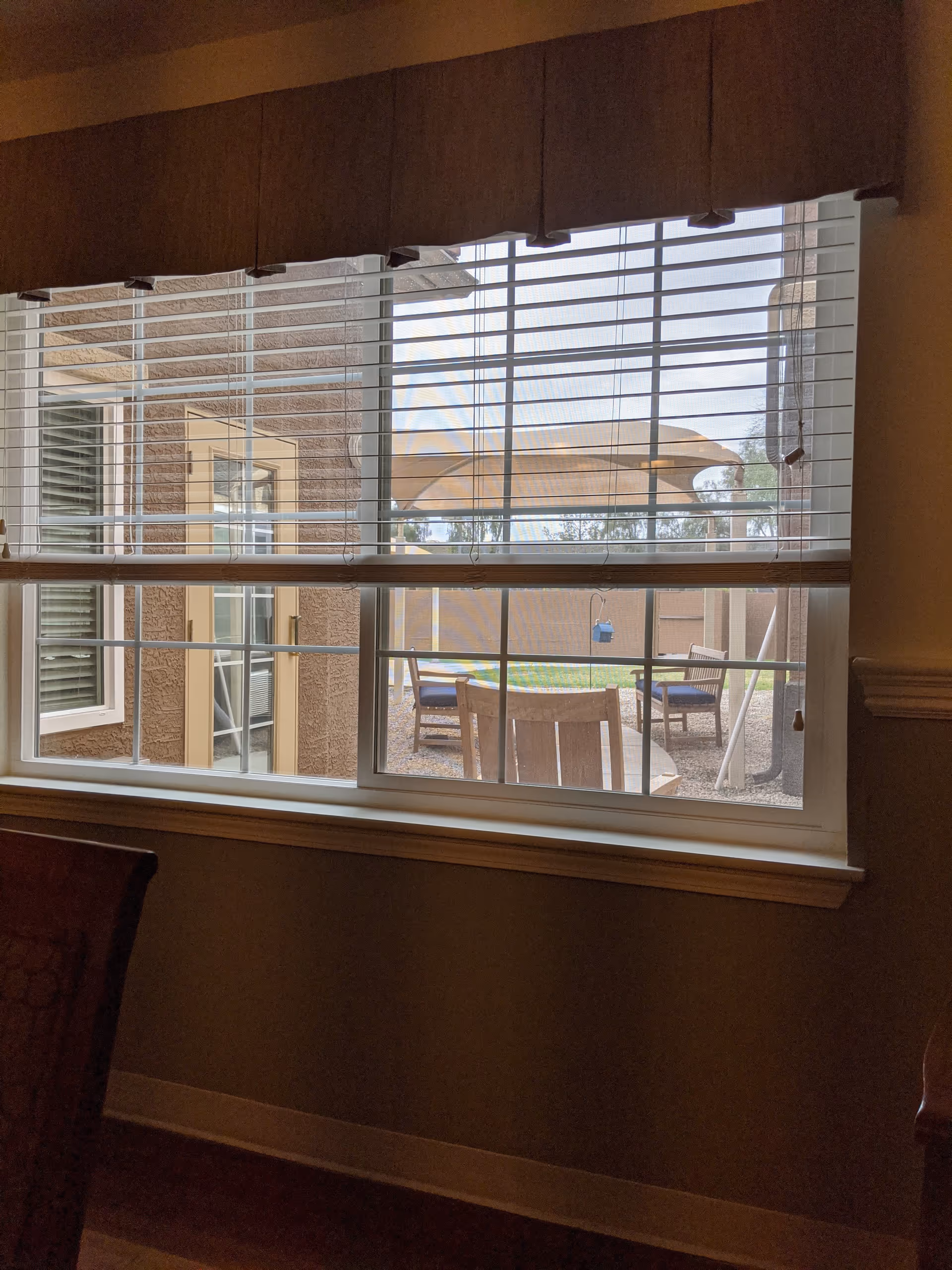 Interior room with a window, blinds, and outdoor patio furniture visible outside.
