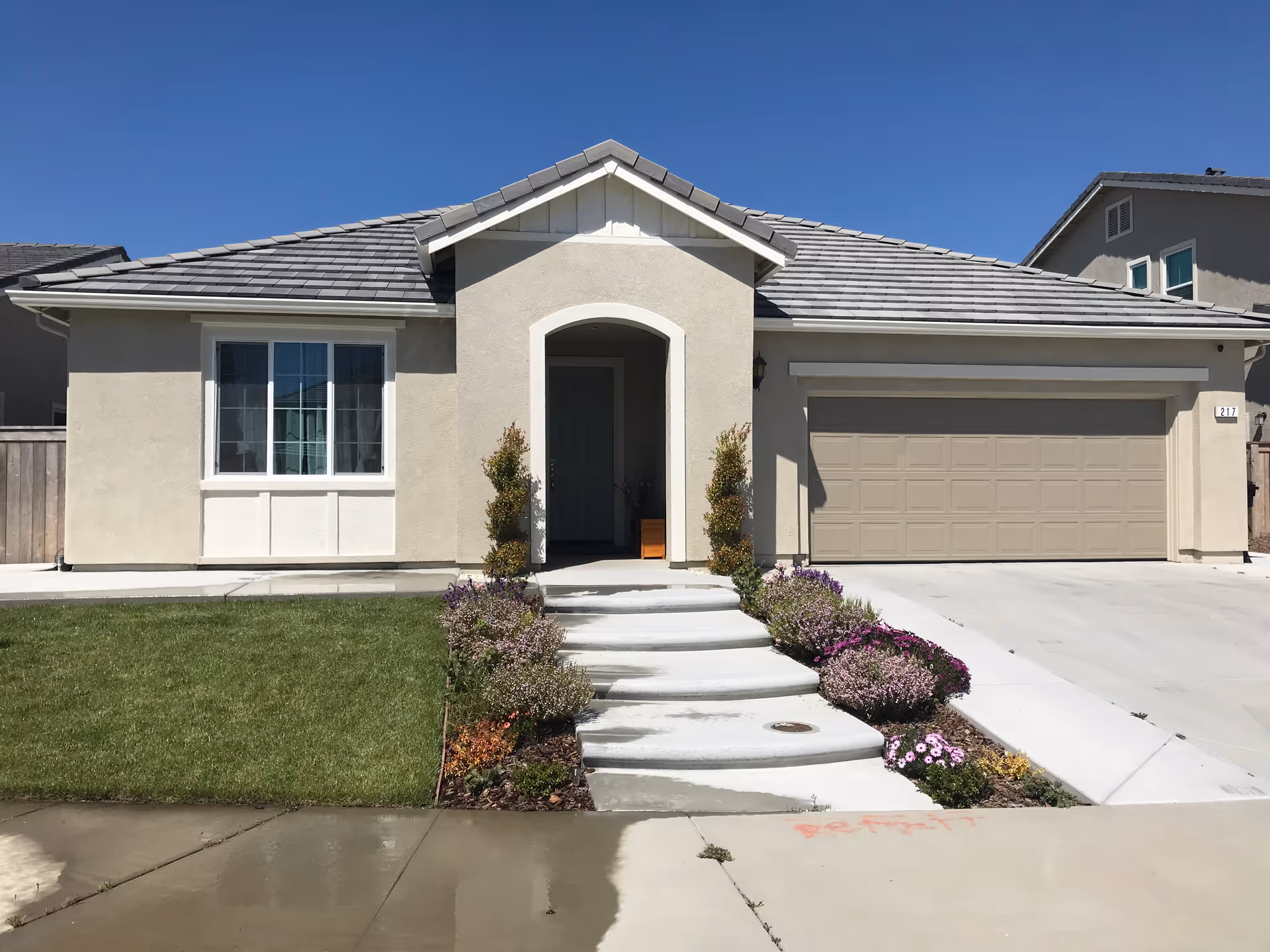 Beige single-story house with arched entry, steps, and attached two-car garage.