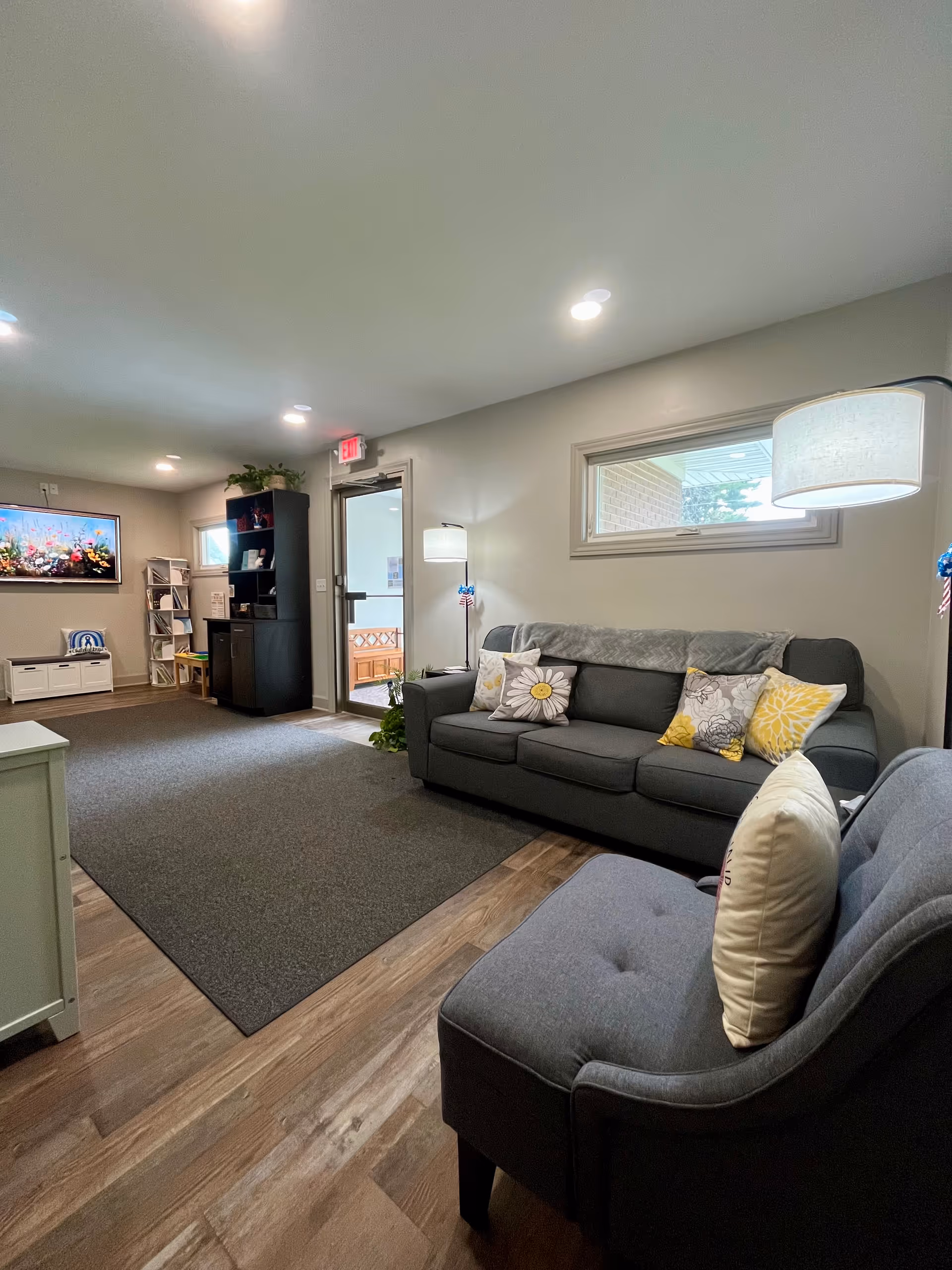 Cozy, well-lit living room with gray sofas, decorative pillows, lamps, and a doorway.