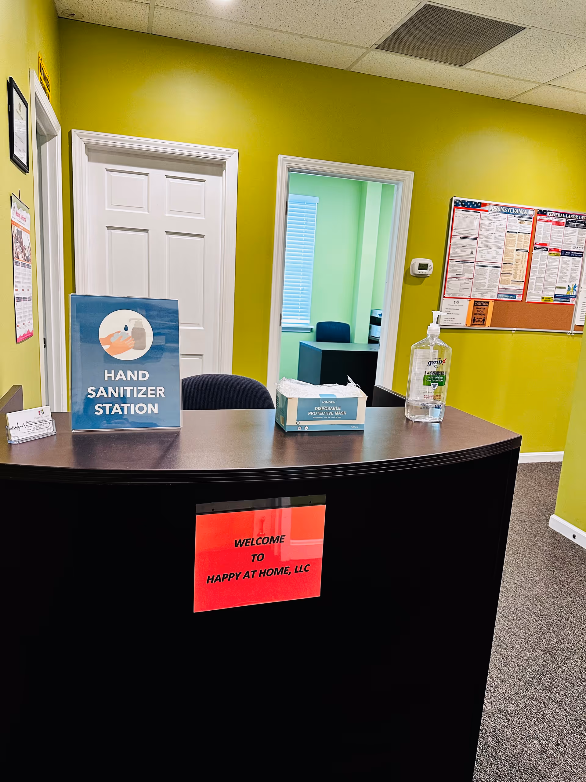 Reception desk in bright green lobby with hand sanitizer station and welcome sign.