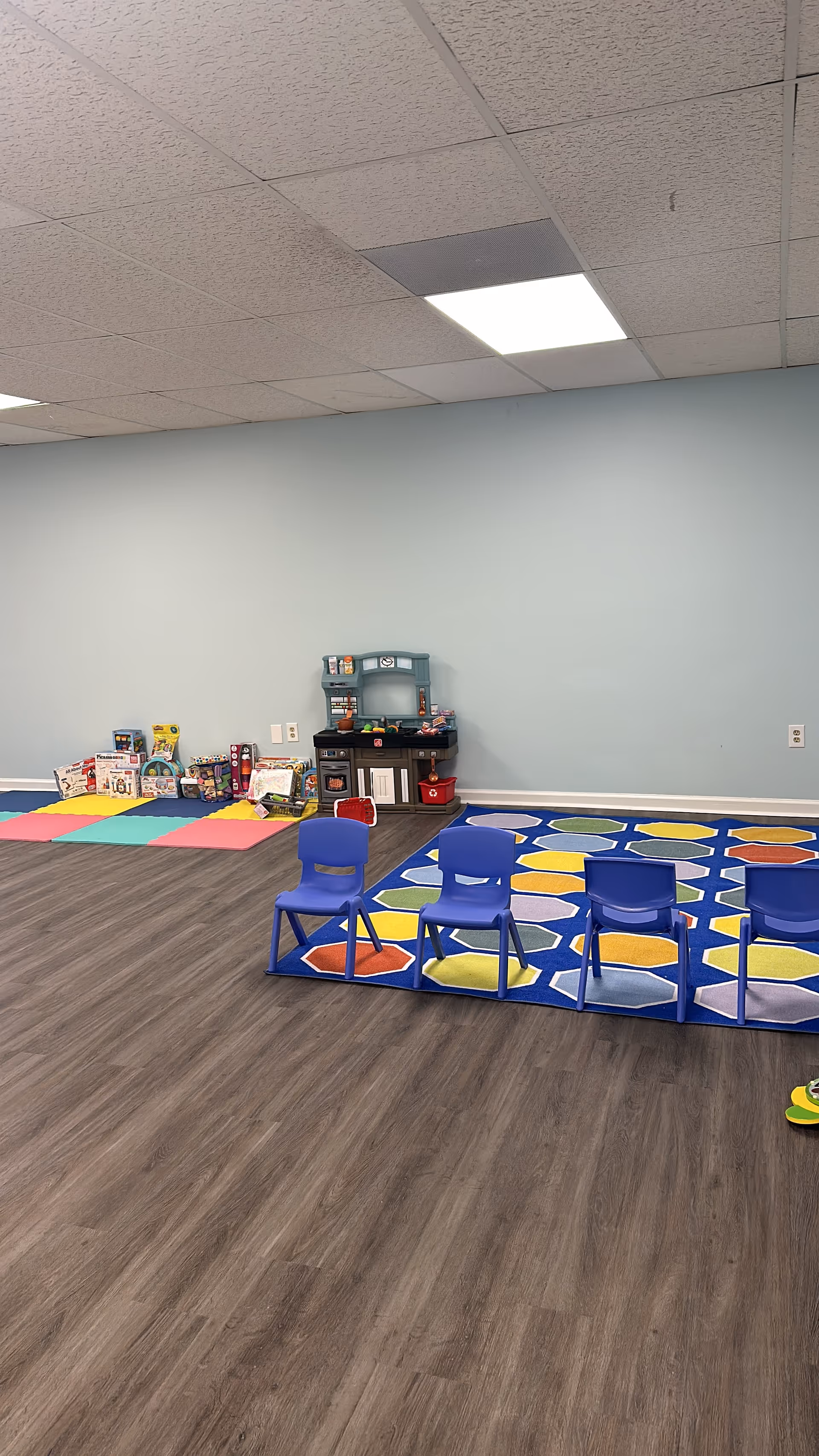 Indoor play area with blue chairs, colorful mats, and toy shelves.