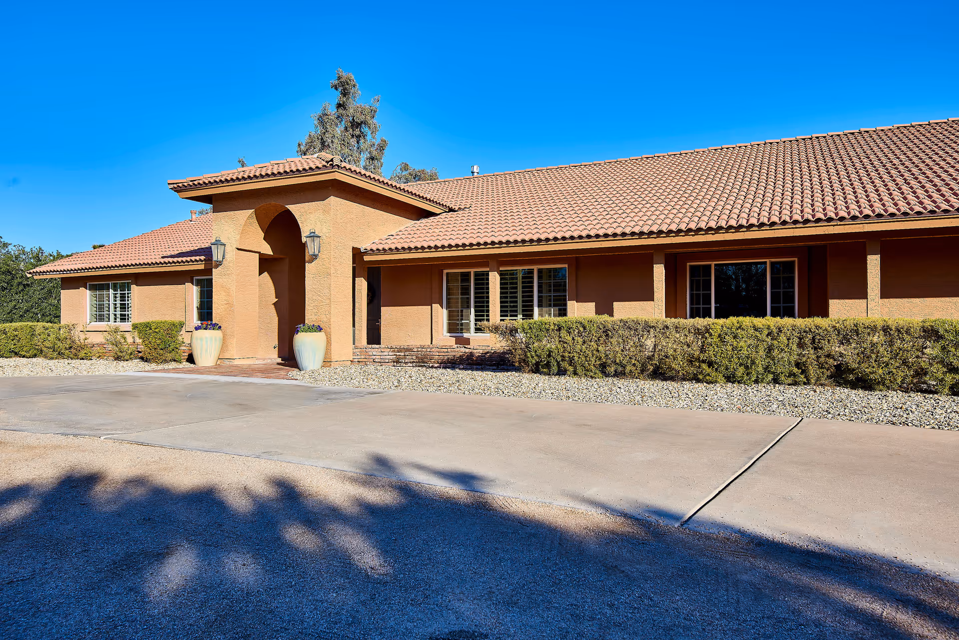 Single-story tan building with red tile roof, arched entrance, and landscaping.