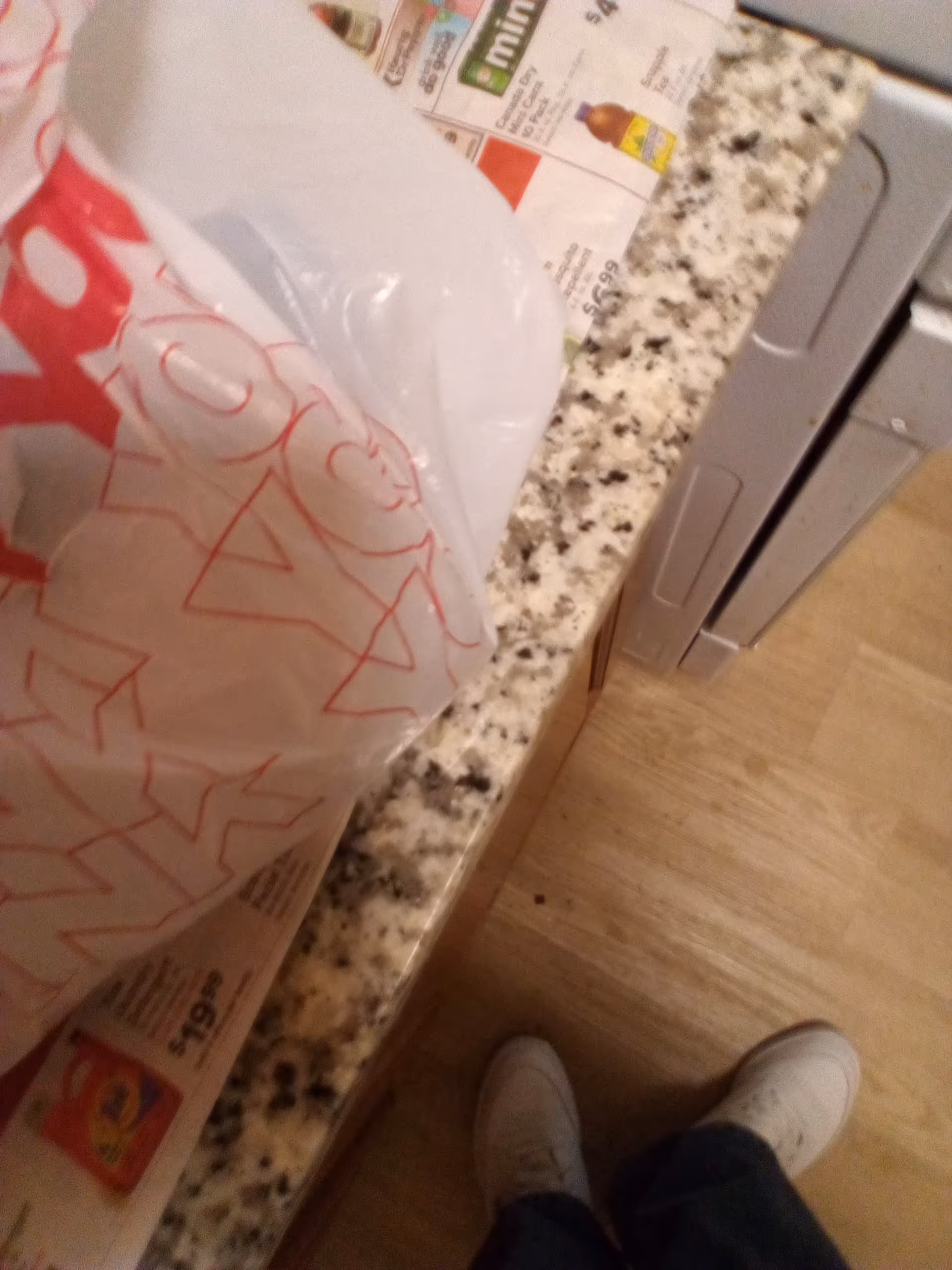 Indoor kitchen counter with granite surface, grocery bags, and a person standing nearby.
