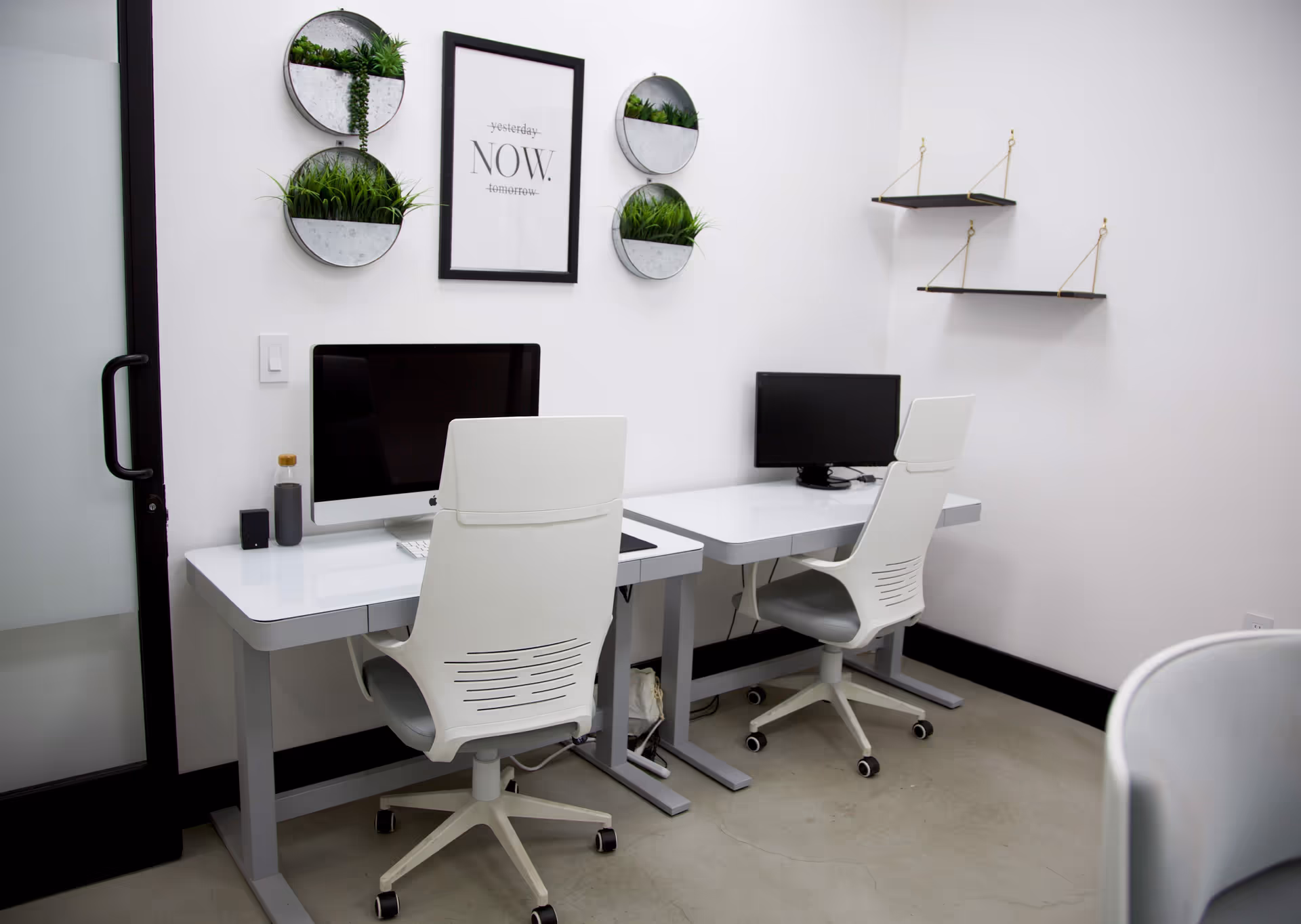 A clean white office area with two desks, chairs, monitors, and circular wall planters