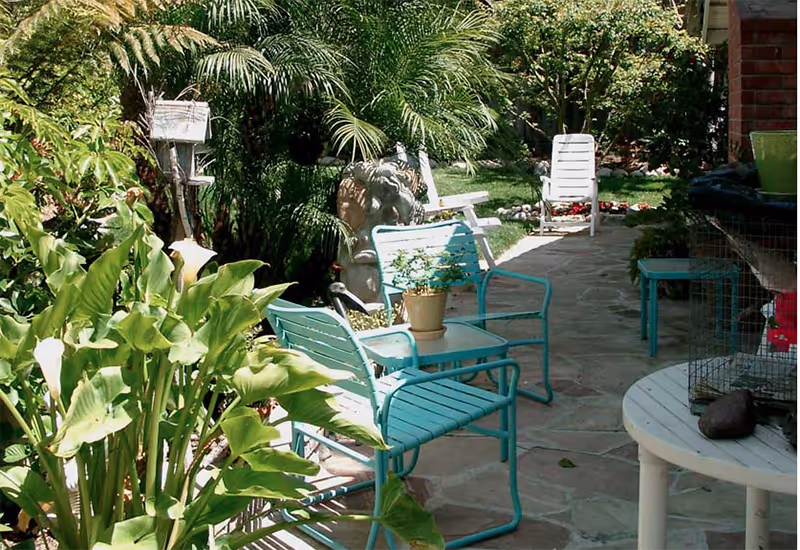 Outdoor patio with teal metal chairs, tables, potted plants, and a stone path.