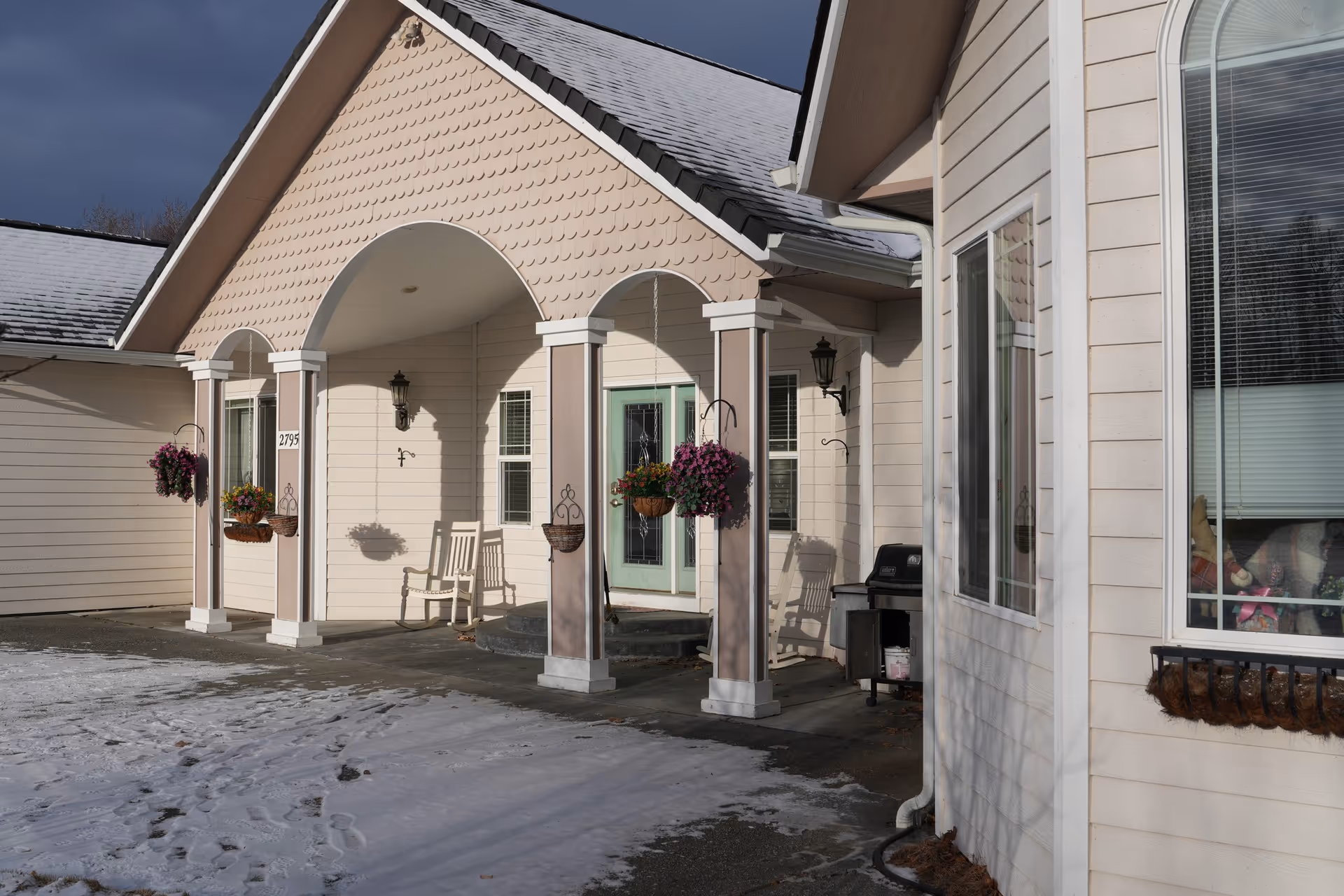 Front exterior of a senior living facility with a covered porch, arches, chairs, and snow.
