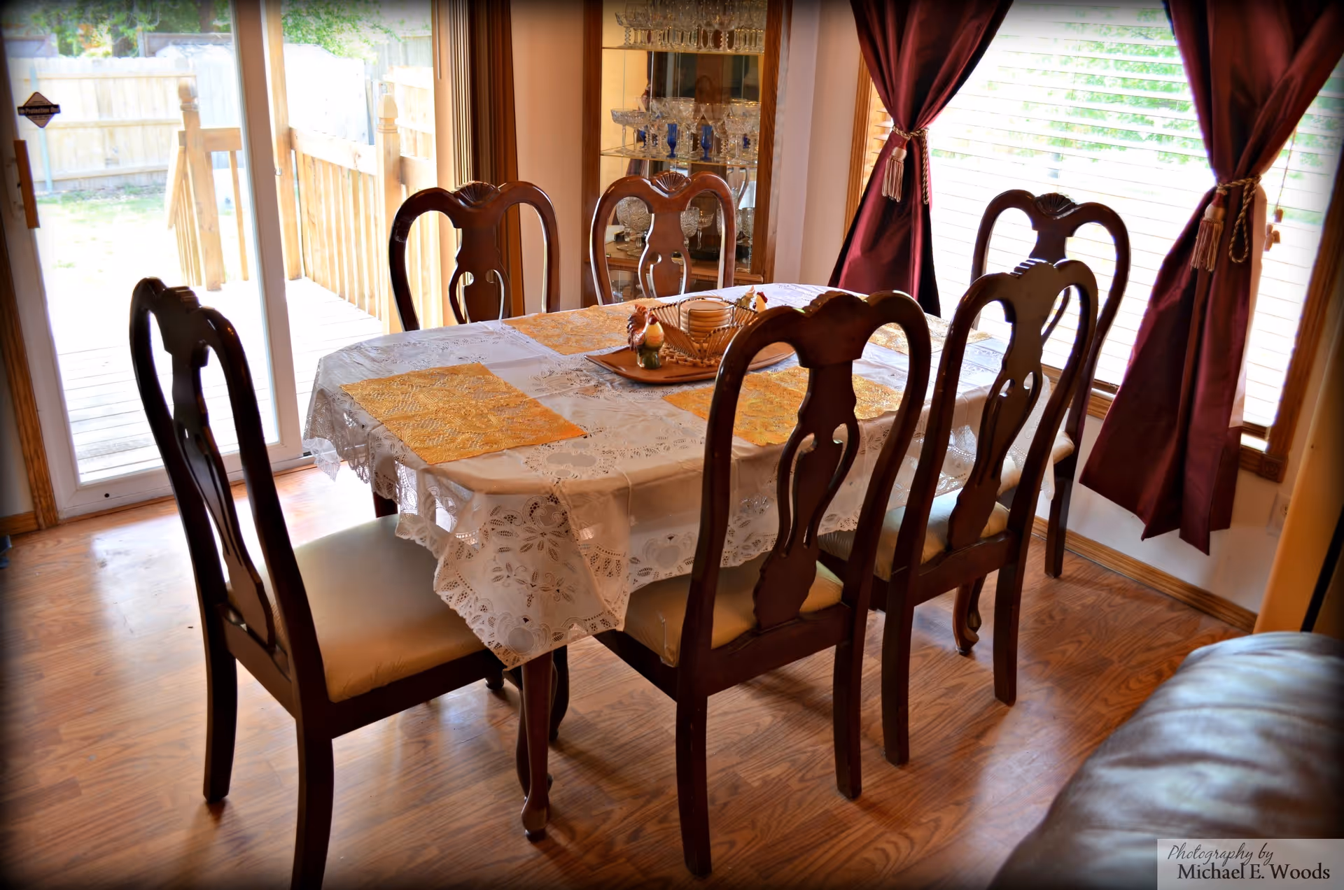 Sunlit dining room with a lace tablecloth and wooden chairs around a large table.