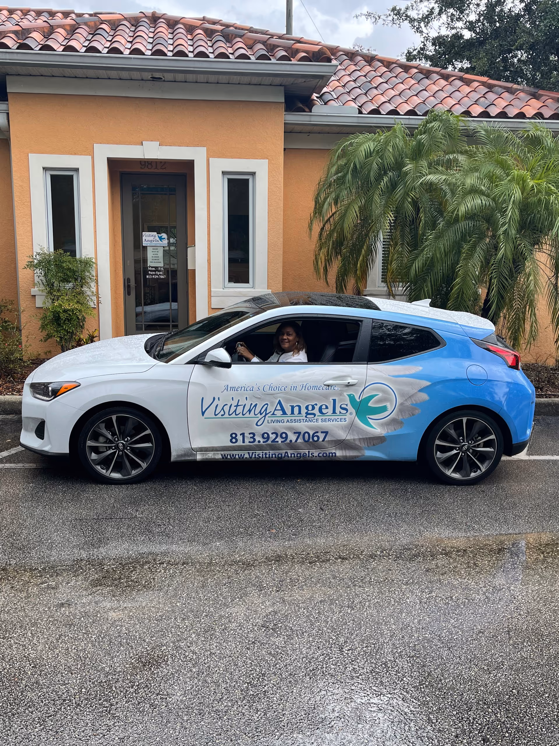 A Visiting Angels-branded car parked in front of a tan building with palm trees