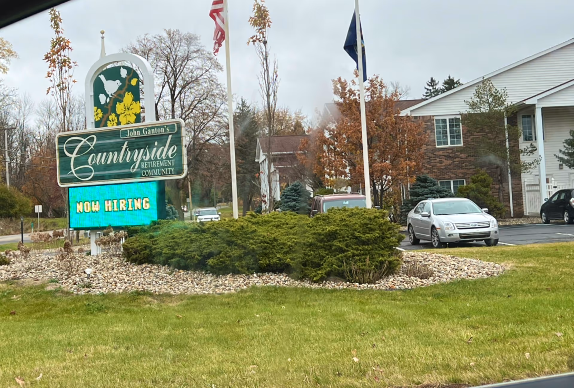Front exterior of Ganton's Countryside Retirement Community sign, building, and parked cars.
