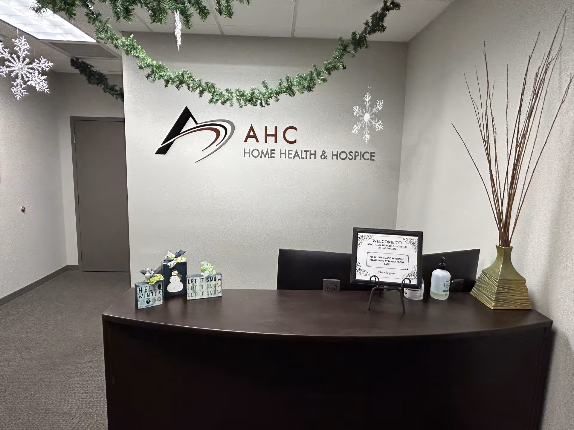 Reception desk in a neutral lobby with AHC Home Health & Hospice sign and holiday decor.