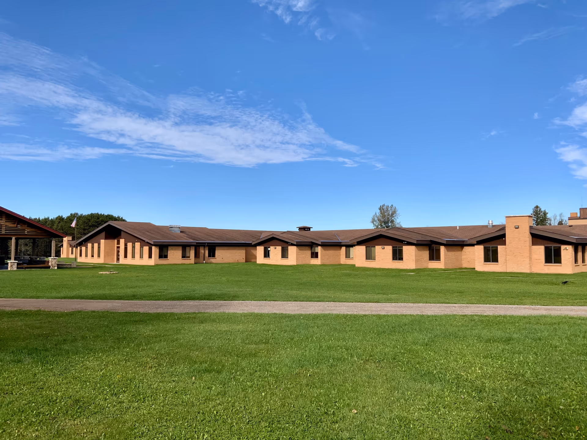 Single-story brick senior care facility with a wide green lawn under a blue sky.