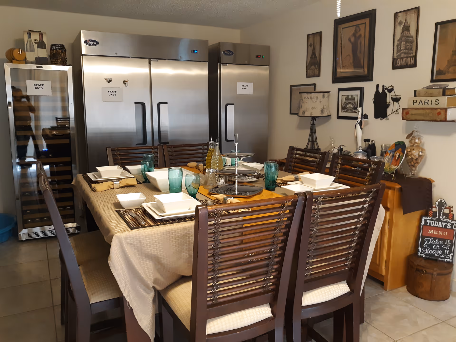 A dining room with a large table set for a meal and stainless refrigerators.