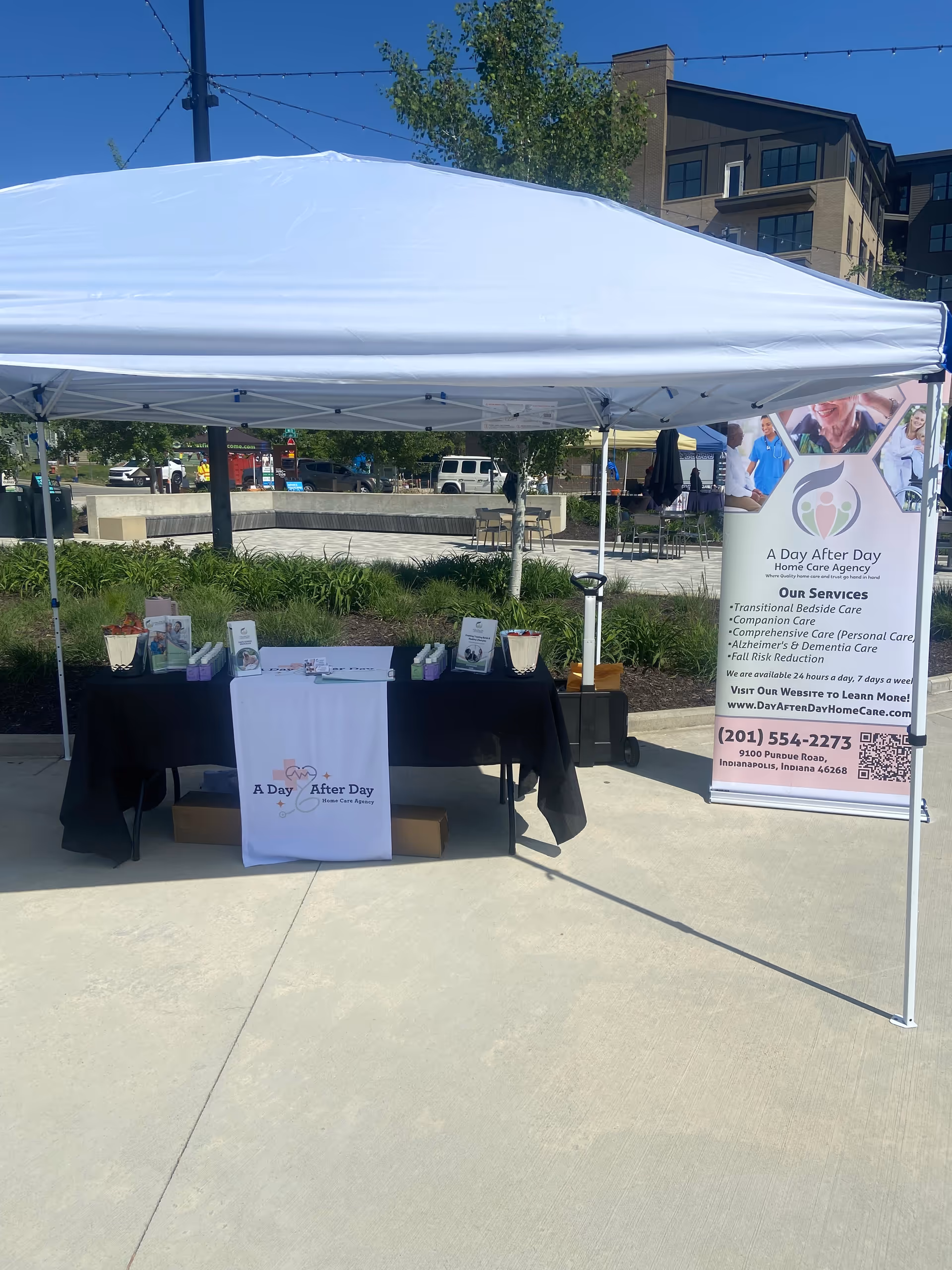Outdoor tent setup with tables displaying information banners for A Day After Day Home Care Agency.