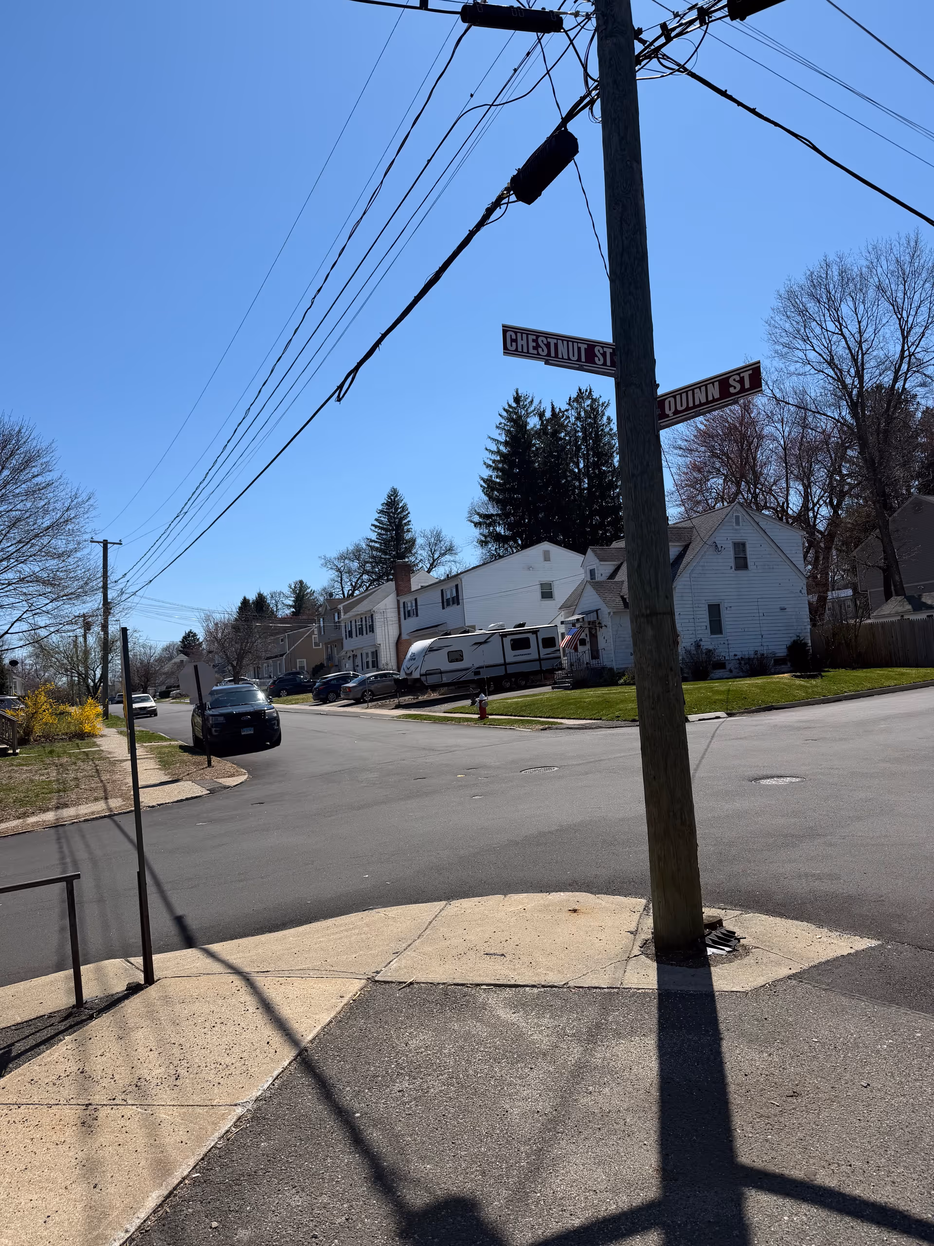 Street intersection with power lines, sidewalk, and residential houses under clear blue sky.