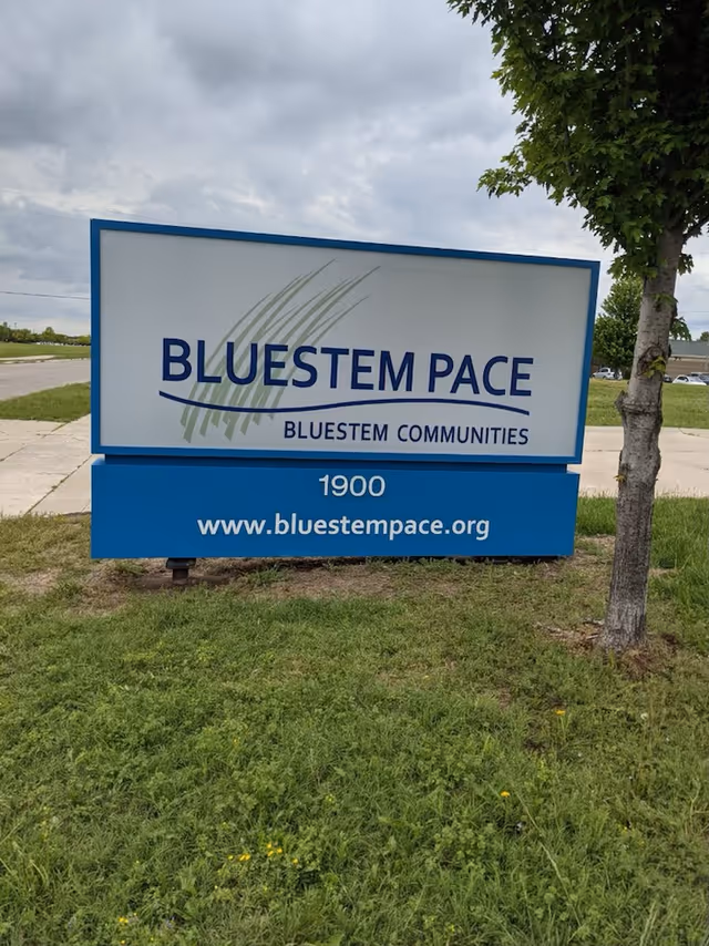Bluestem PACE sign on grassy lawn beside a tree near the road