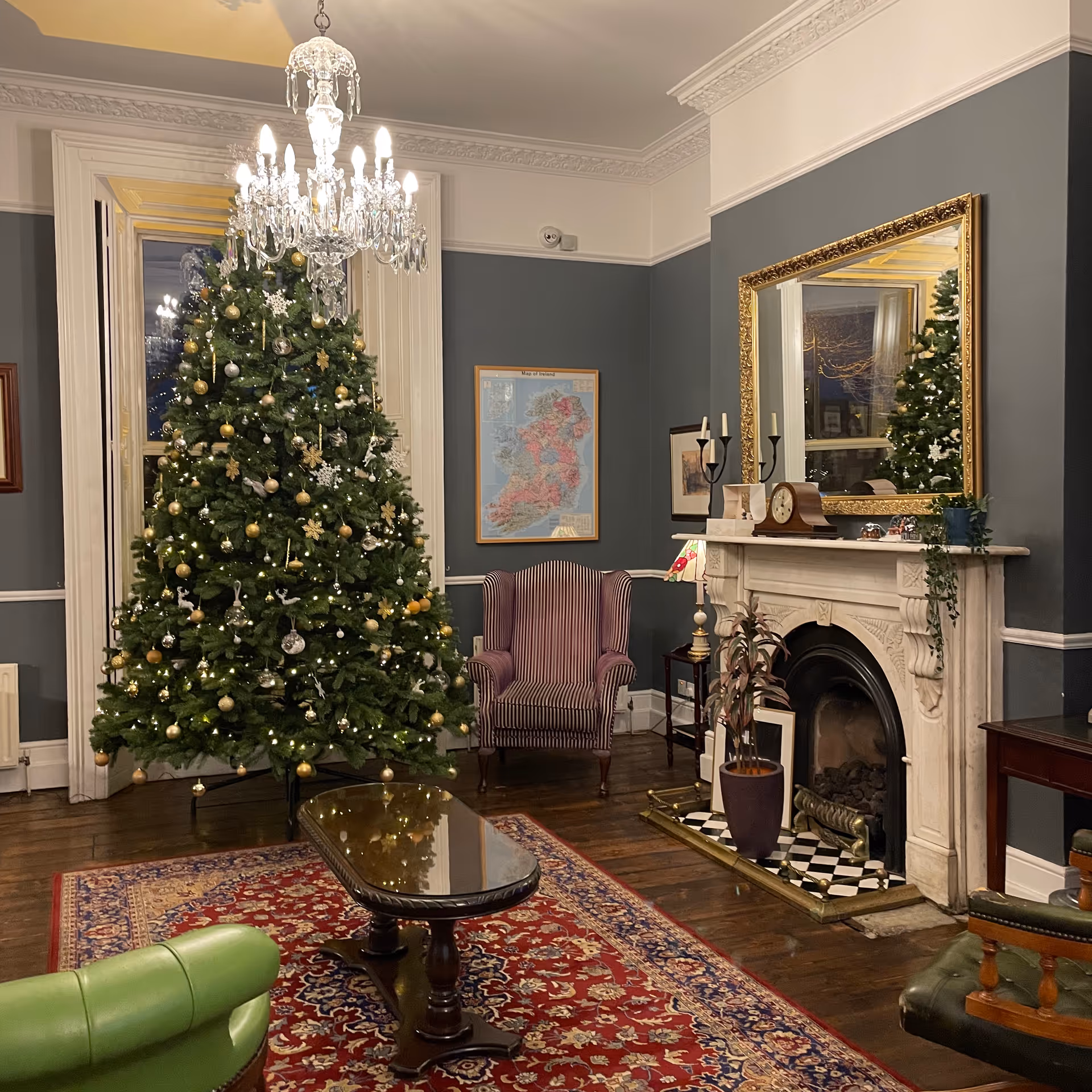Elegant living room with a tall Christmas tree, chandelier, marble fireplace, and classic seating.