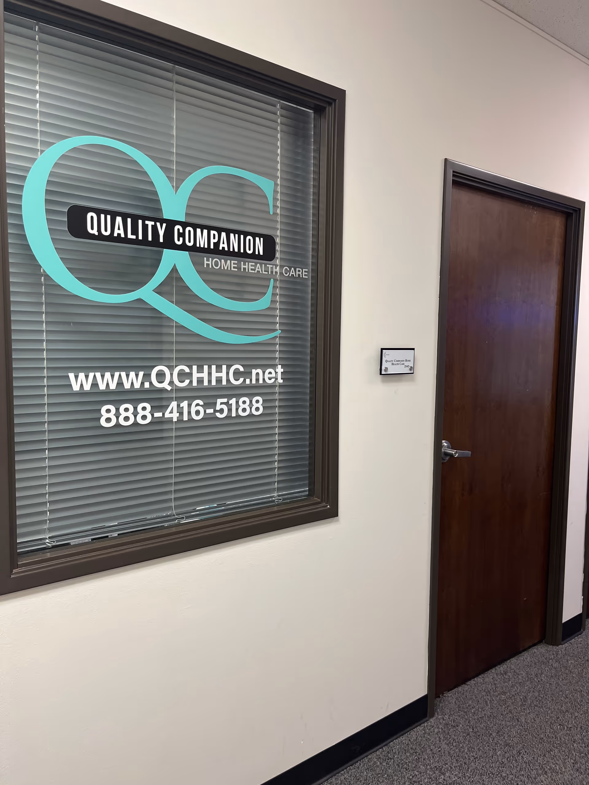 Interior hallway with a large window sign reading Quality Companion Home Health Care and contact info.