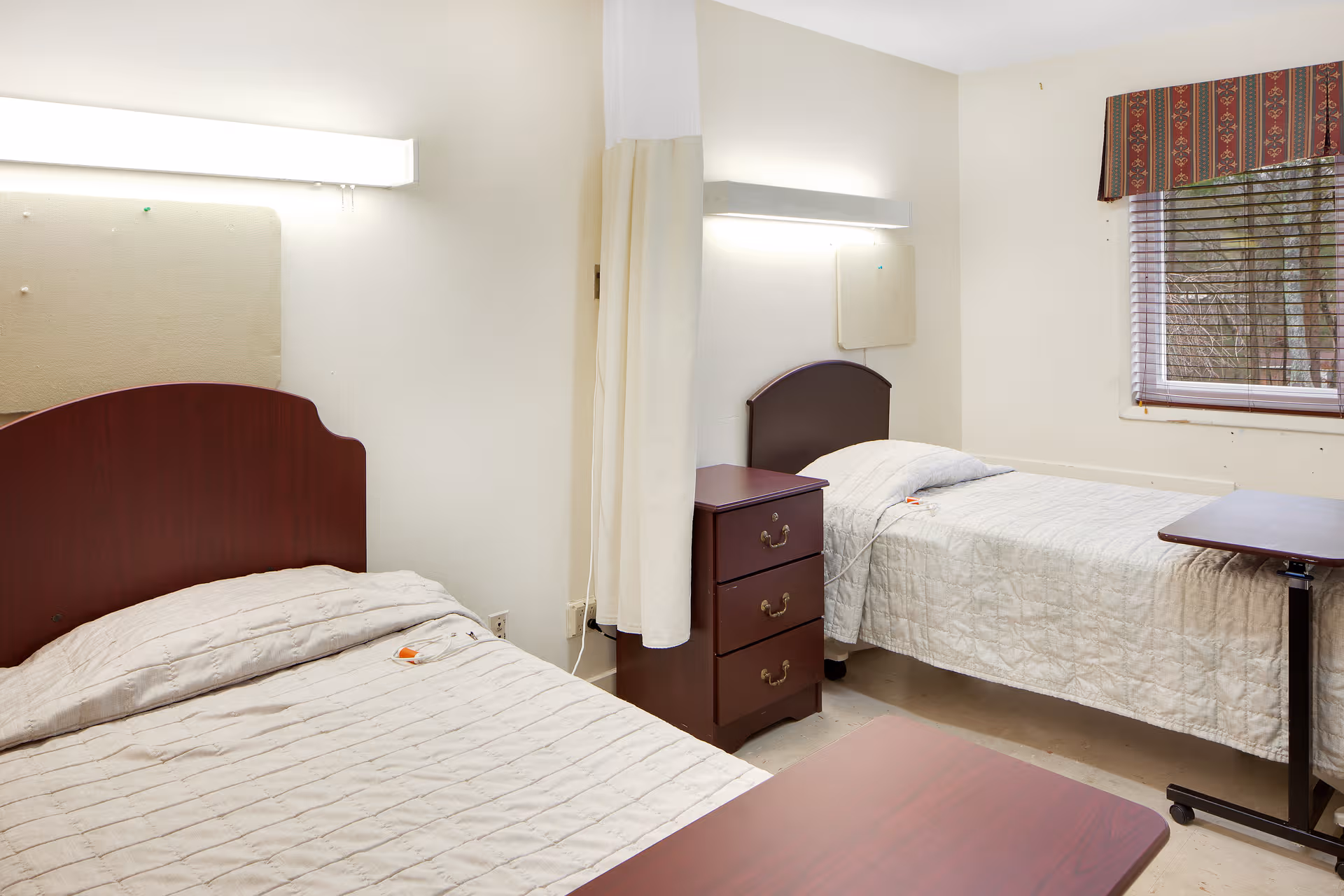 Two single beds with matching quilts, a nightstand, and window in a shared bedroom.