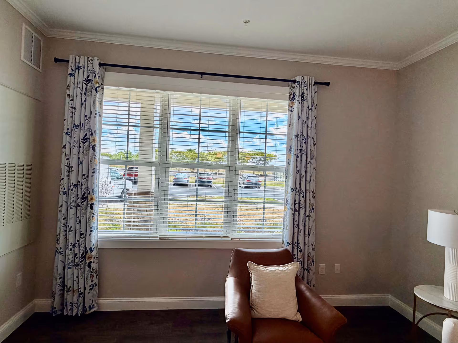 Armchair with a pillow beside a window and floral curtains in a cozy living room.