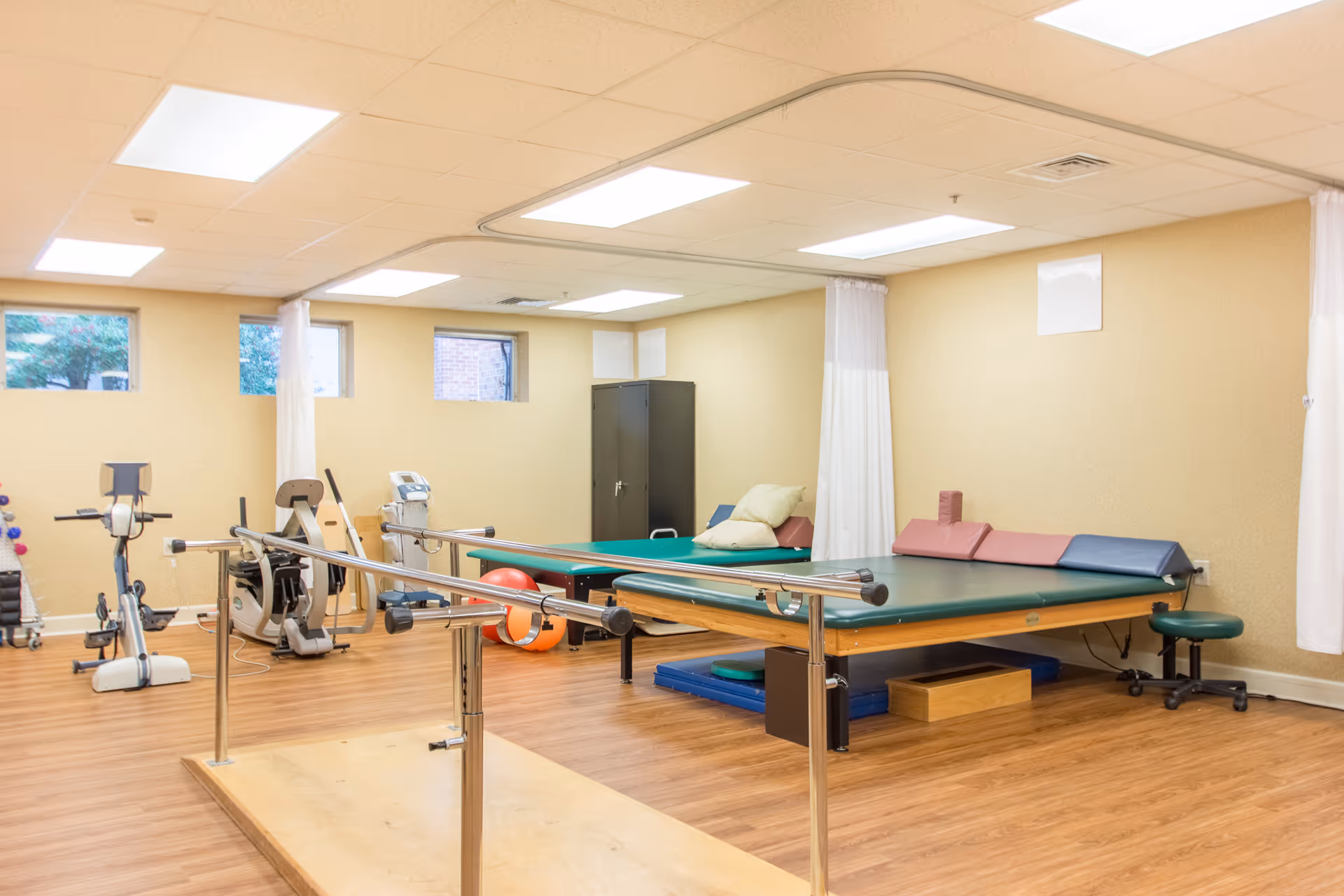 Interior rehabilitation room with exercise equipment, mats, and therapy bars.