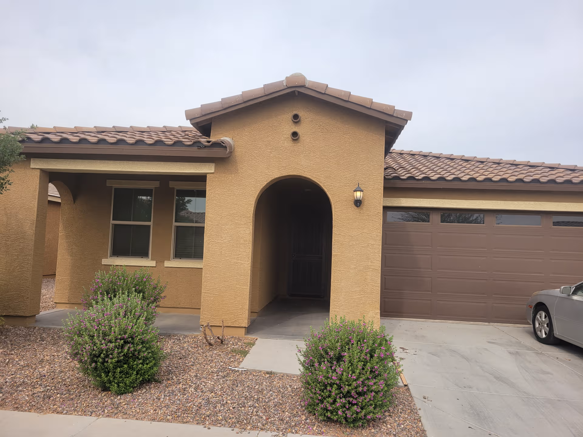 Front view of a tan stucco assisted living building with arched entry.