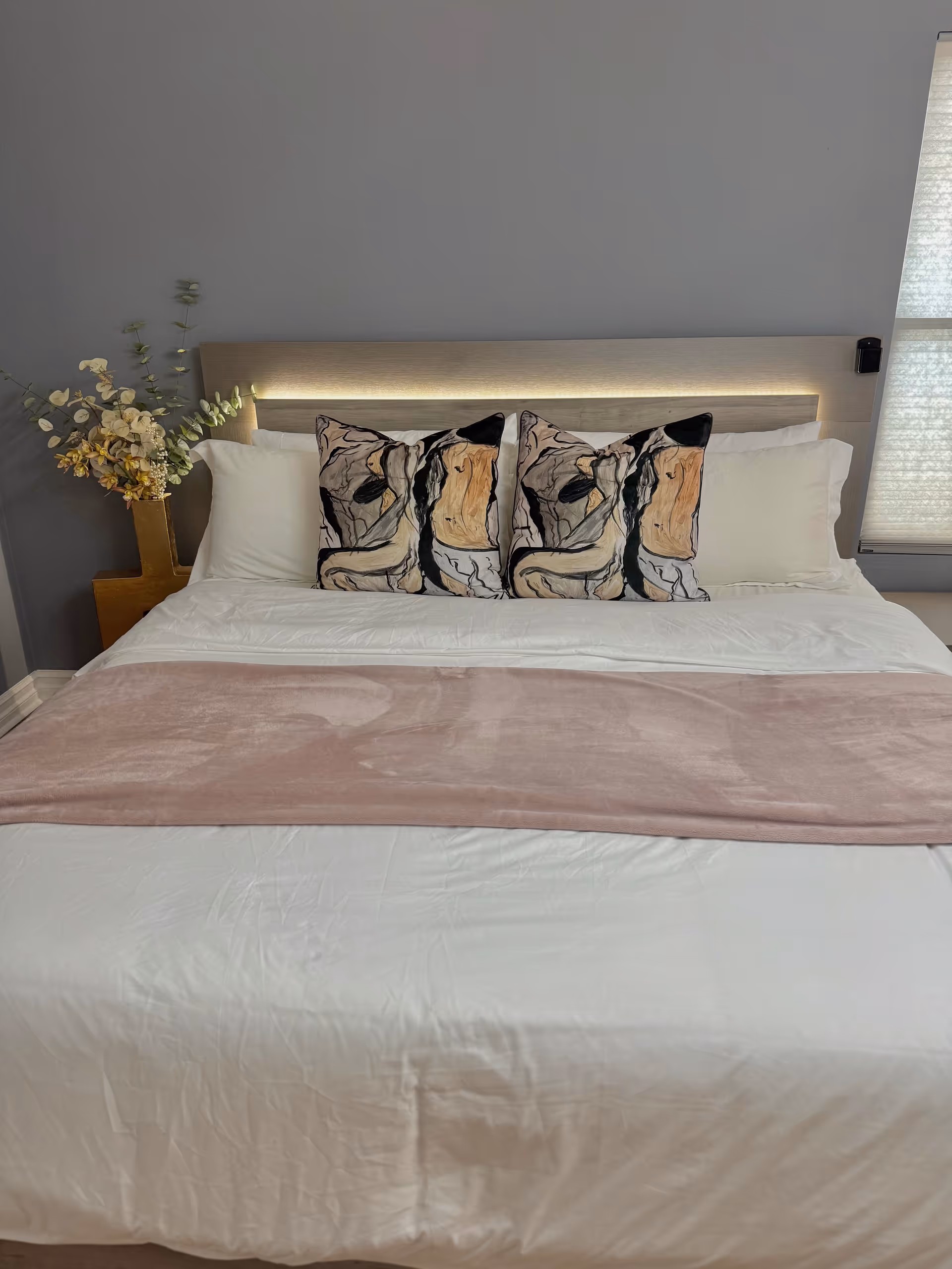 A neatly made bedroom featuring a bed, three decorative pillows, and a pink throw.