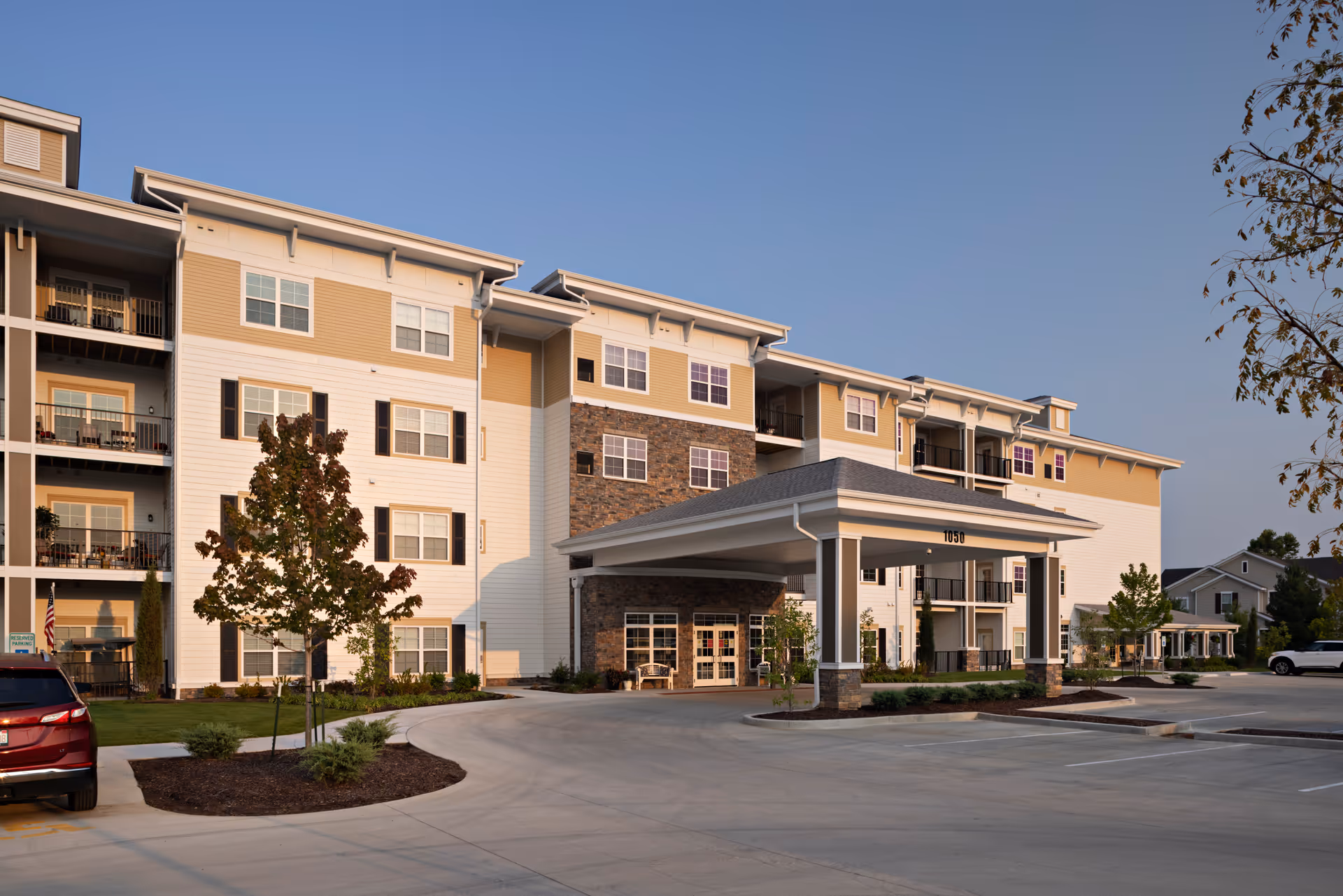 Exterior front of a multi-story senior living building with a covered porte-cochere entrance, balconies, and adjacent parking area.