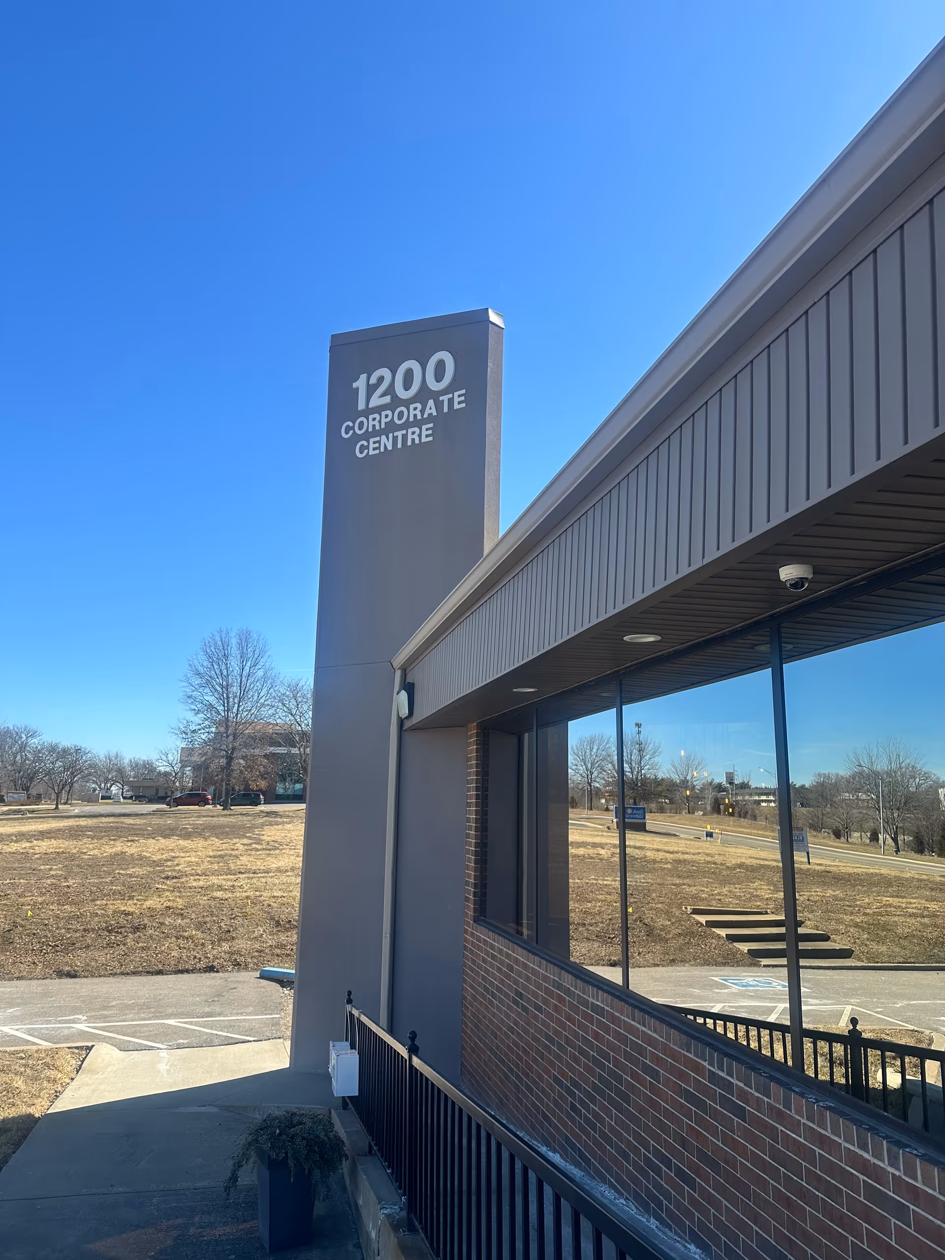 Exterior view of a building with a tall sign reading 1200 Corporate Centre and glass windows.