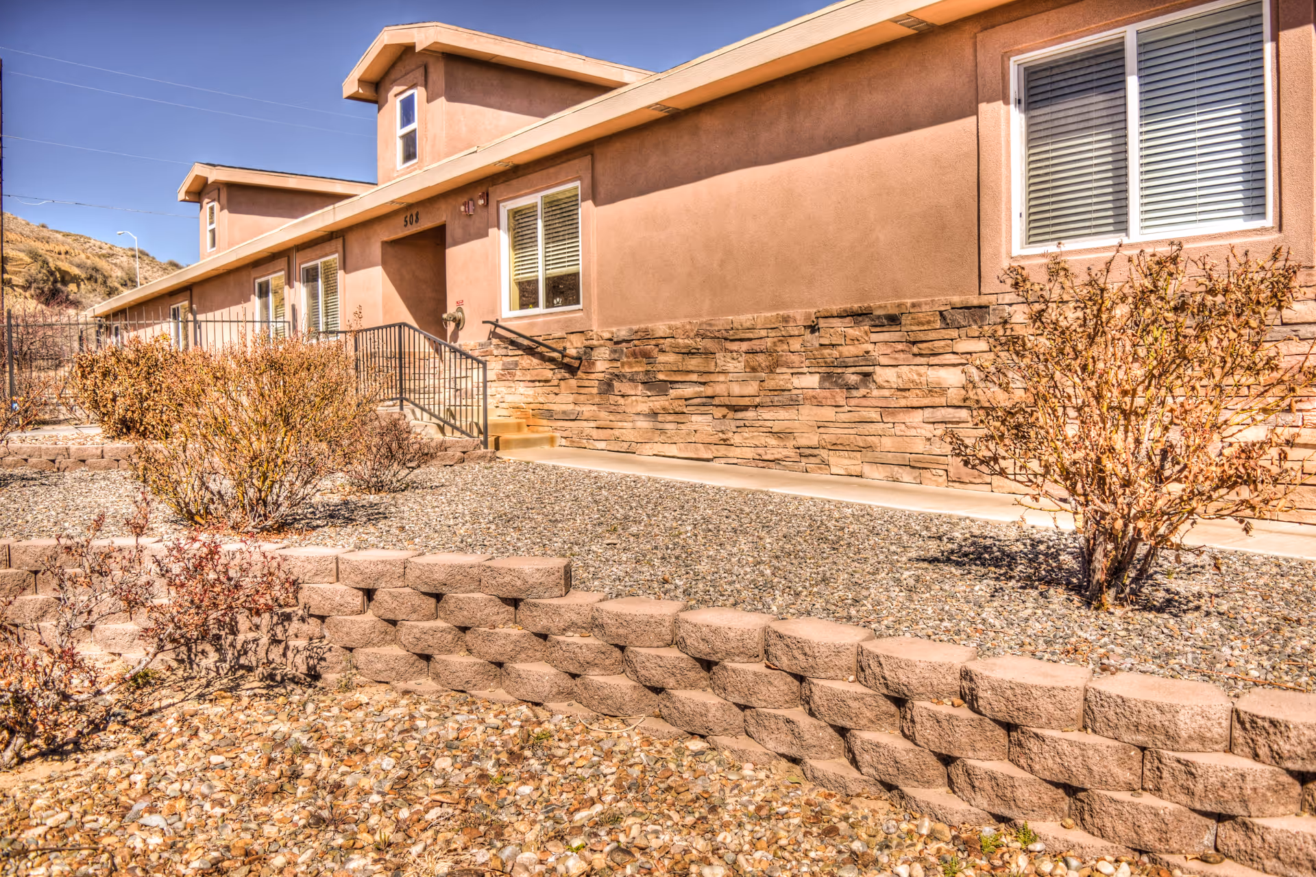 Exterior view of BeeHive Homes of Farmington facility with stucco walls, stone accents, desert landscaping.