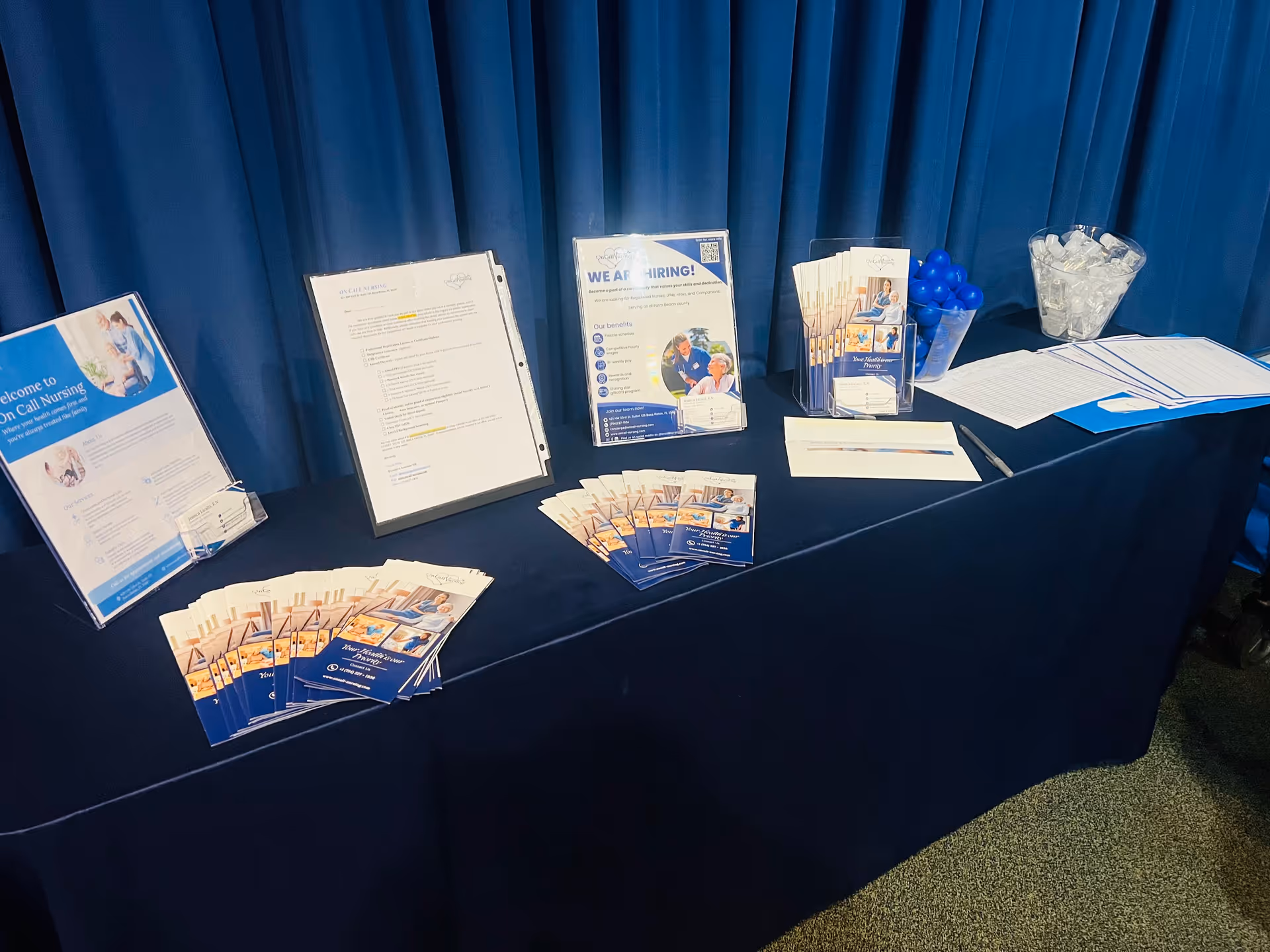 A blue-draped table holds brochures at a recruitment booth.