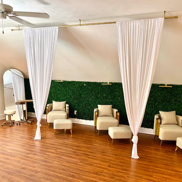 Salon-like sitting area with white curtains, green wall, and beige chairs on wooden floor.