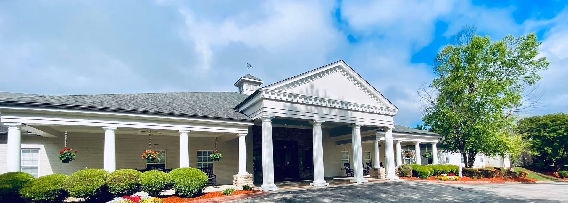 Front exterior of a white, columned SummerHouse Byrd Springs senior living facility with landscaped entry.